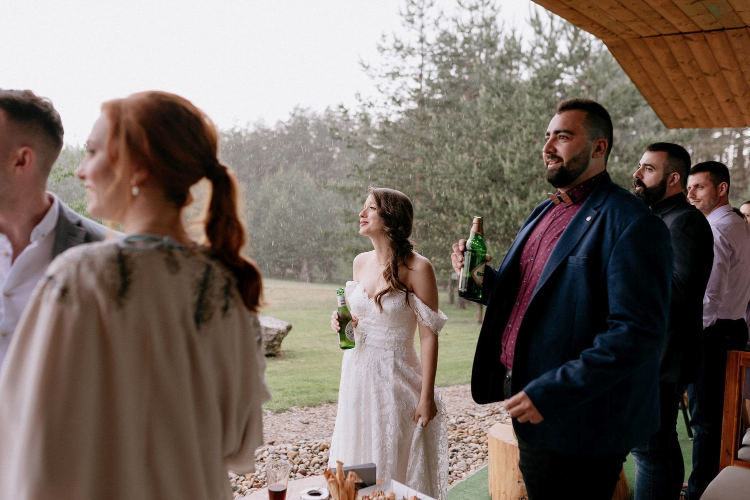 Wedding guests gather under a rustic wooden pavilion during an outdoor celebration.