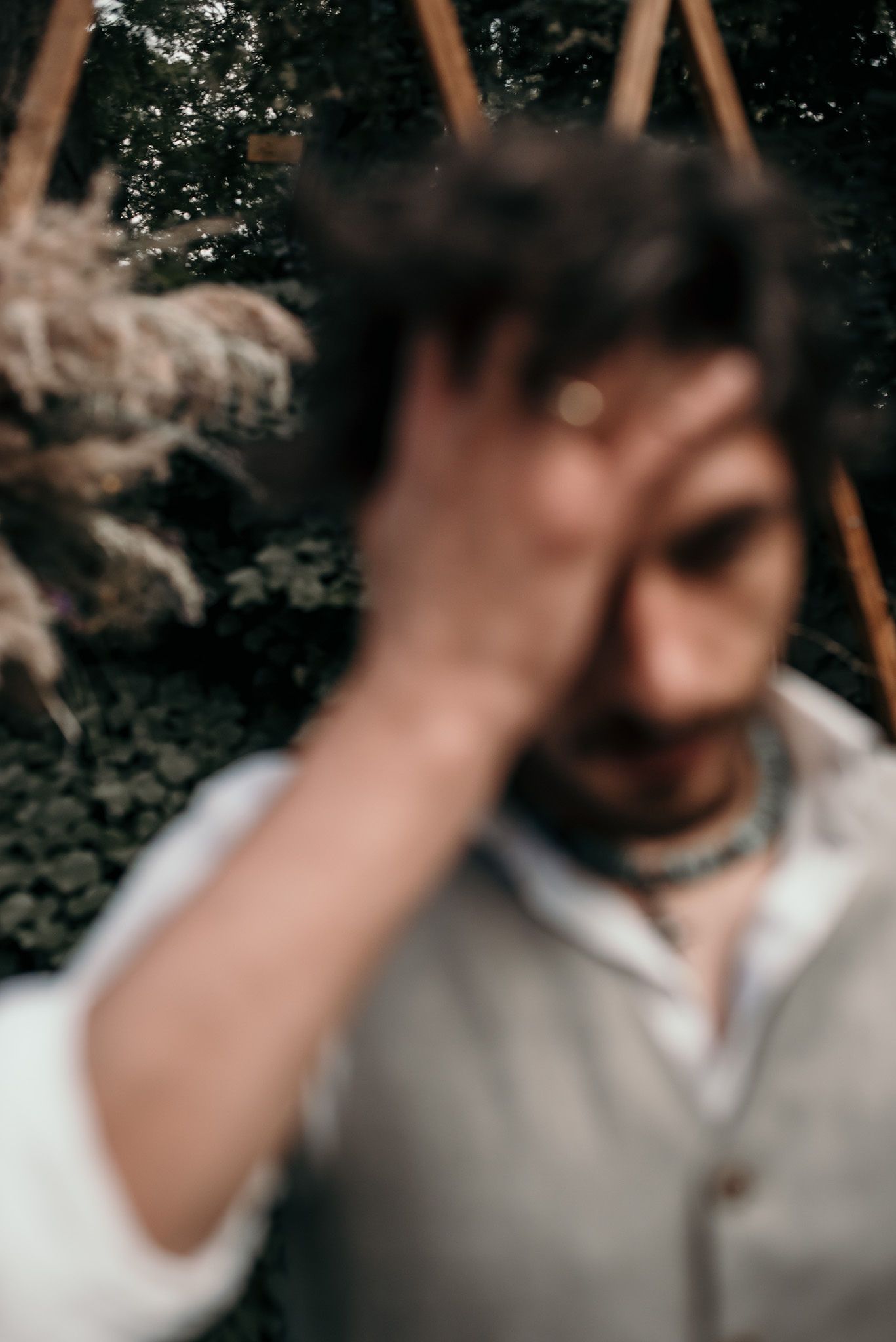 A moody portrait showing a person in a gray vest looking downward in a natural outdoor setting.