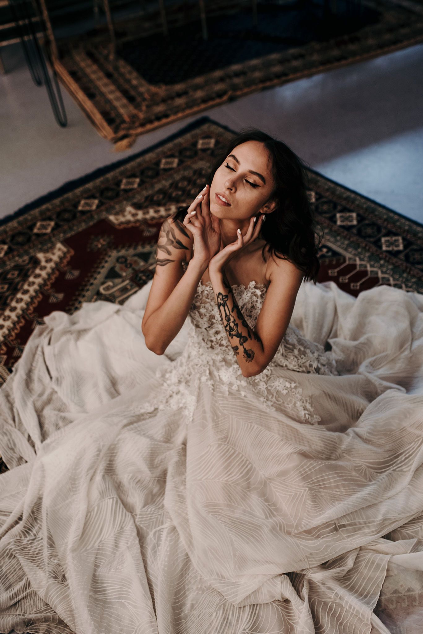 Dramatic bridal pose on patterned carpet showing flowing white wedding gown with lace details.