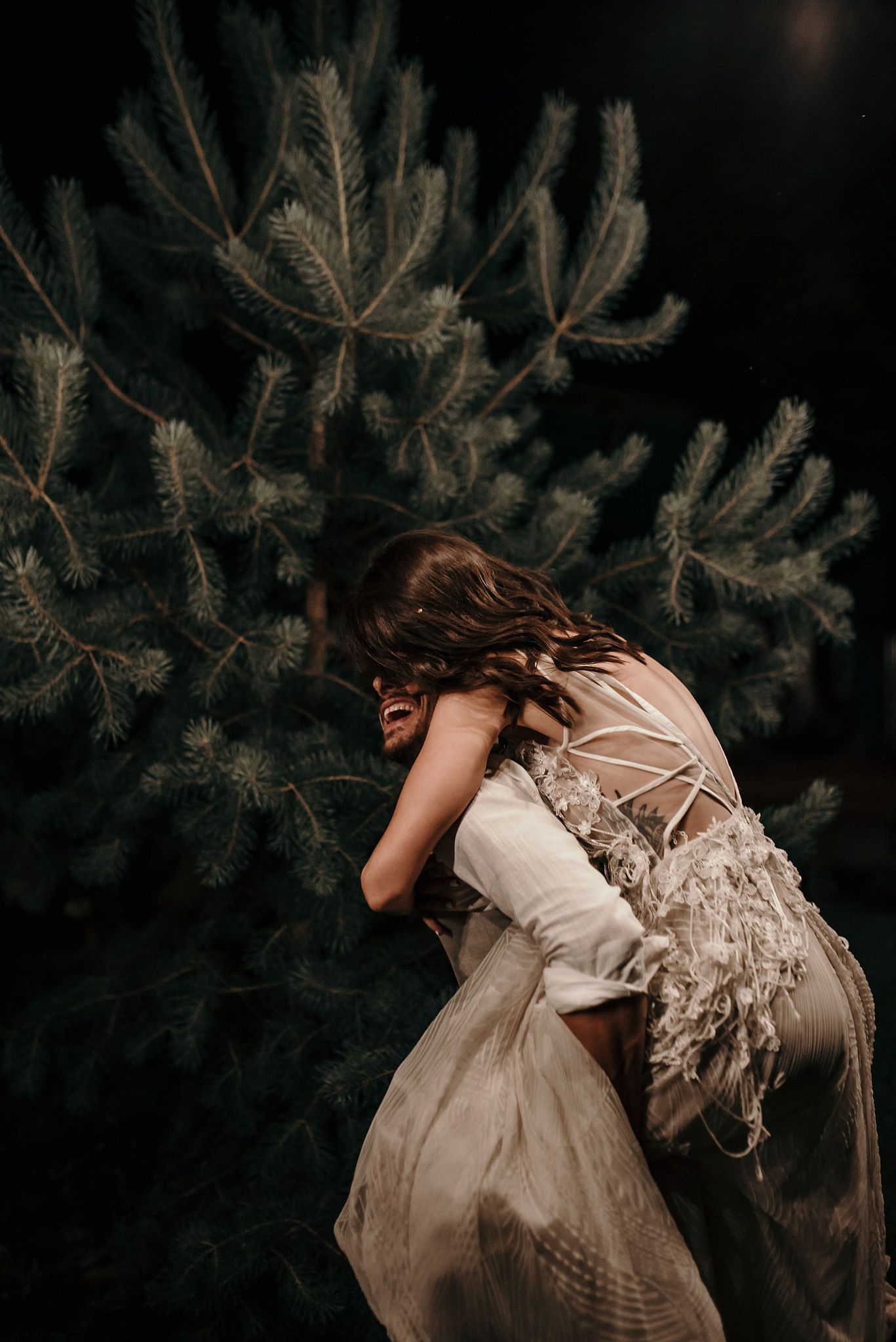 A series of moody photographs showing a person in a vintage dress moving through dark pine branches in an artistic sequence.