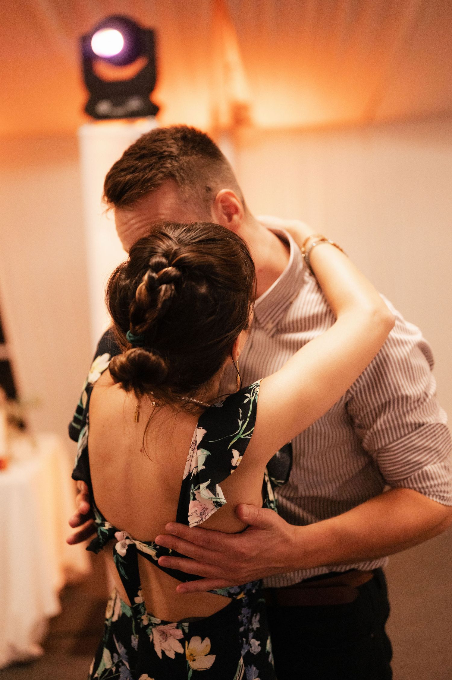 A couple dances together in an intimate embrace with warm orange lighting creating a romantic atmosphere.