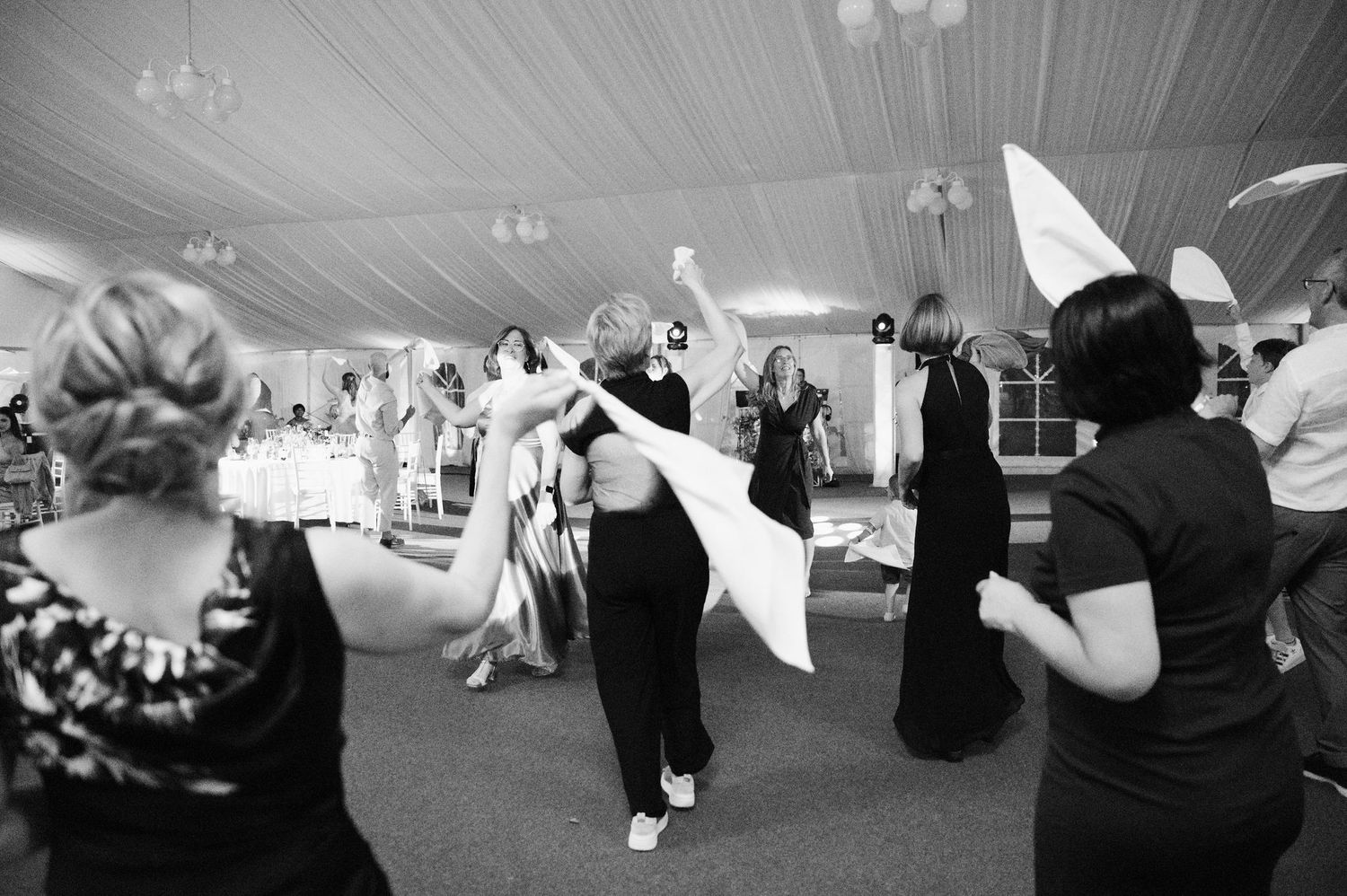 Black and white photo showing silhouettes of wedding guests dancing in a reception tent.