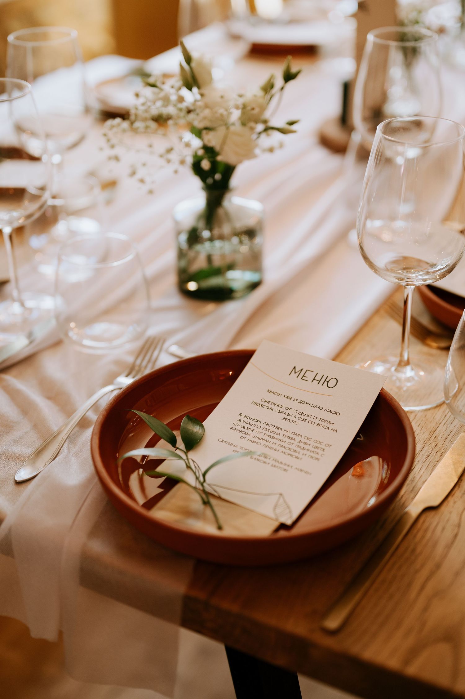 Close-up of table setting with menu card, terracotta plates, and delicate floral accents.