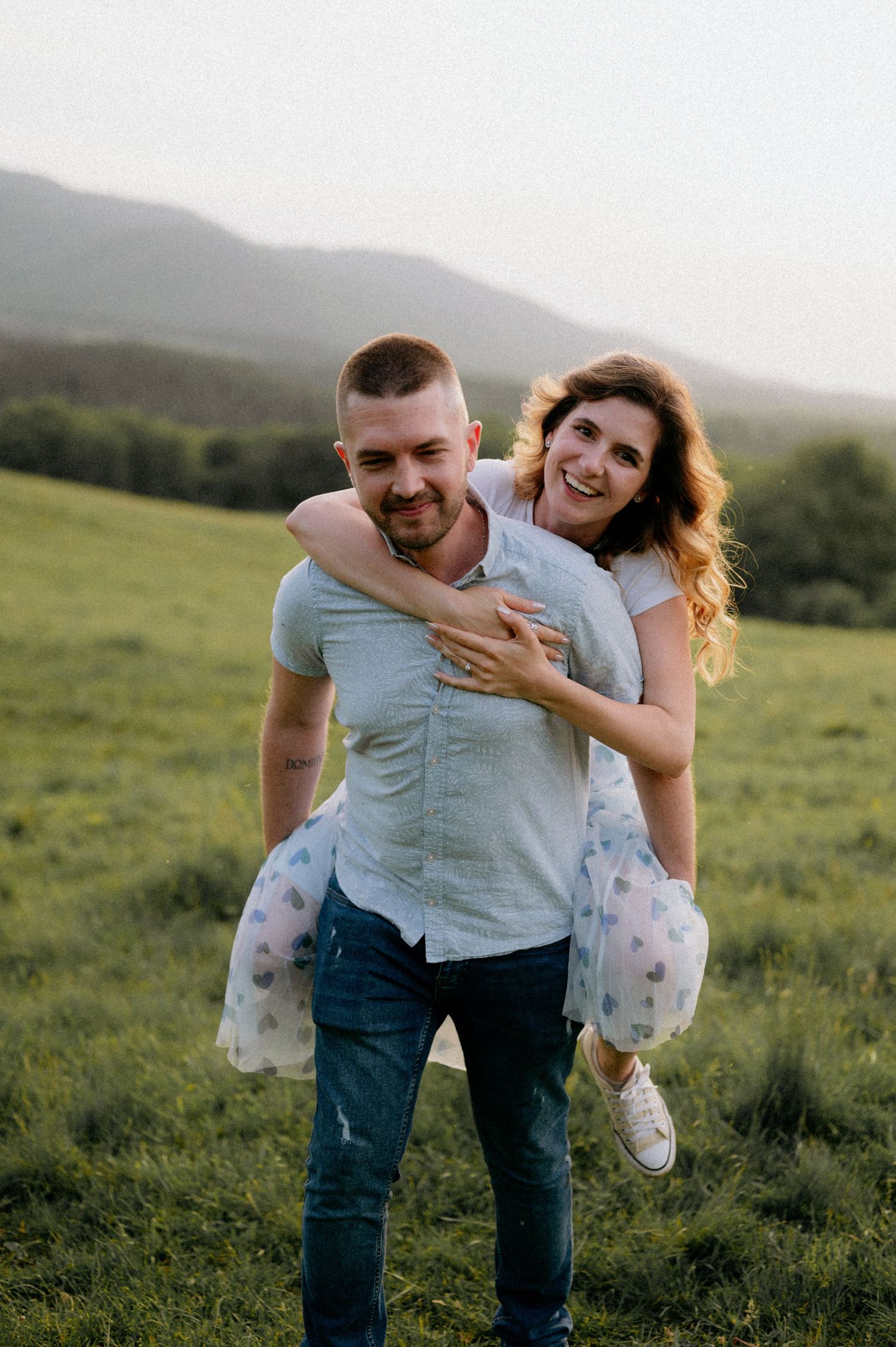 Playful couple sharing a piggyback ride in a green mountain meadow.