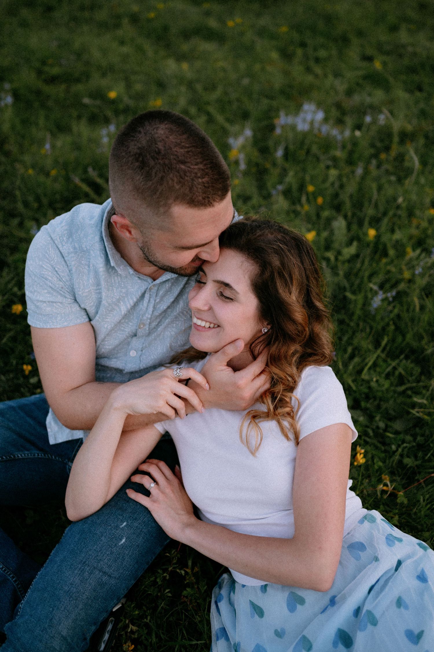 Happy couple sharing loving moments on a grassy hillside with wildflowers.
