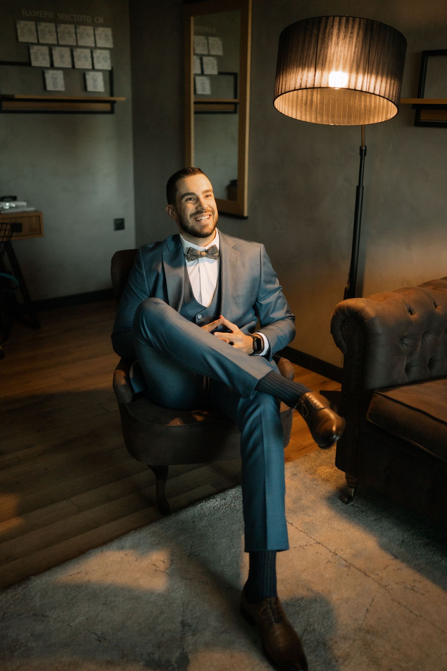 A person in a blue suit sits thoughtfully in a dimly lit room under a pendant lamp creating a moody atmosphere.