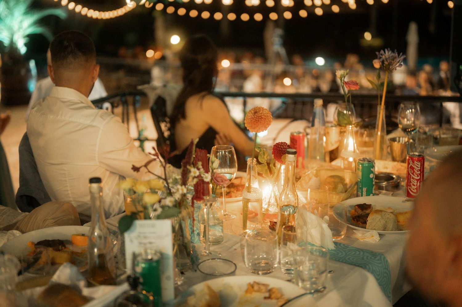 Elegant wedding reception table settings with glowing candles and floral centerpieces in warm ambient lighting.