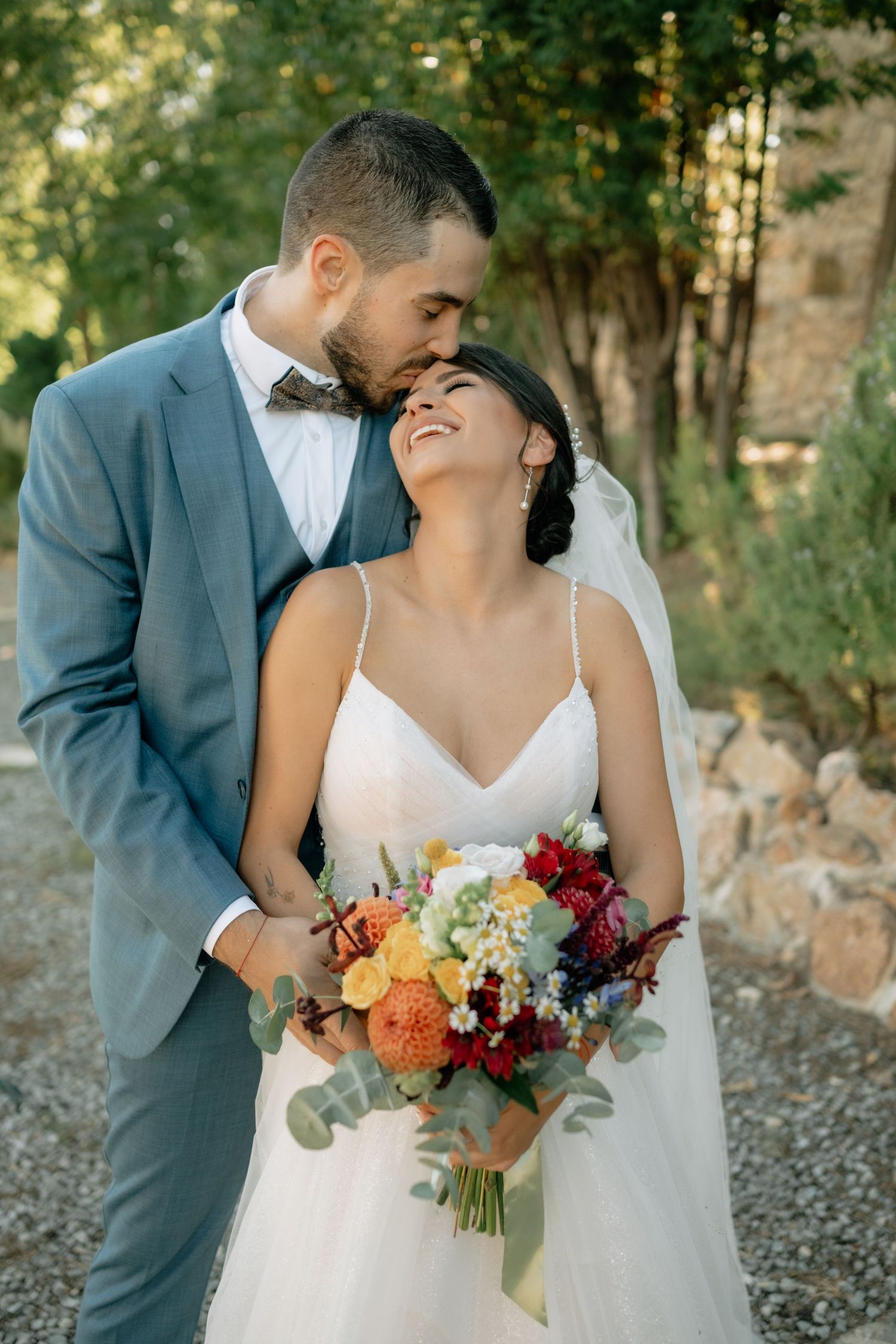 Romantic wedding couple poses outdoors with vibrant autumn bouquet featuring burgundy, orange and white flowers.