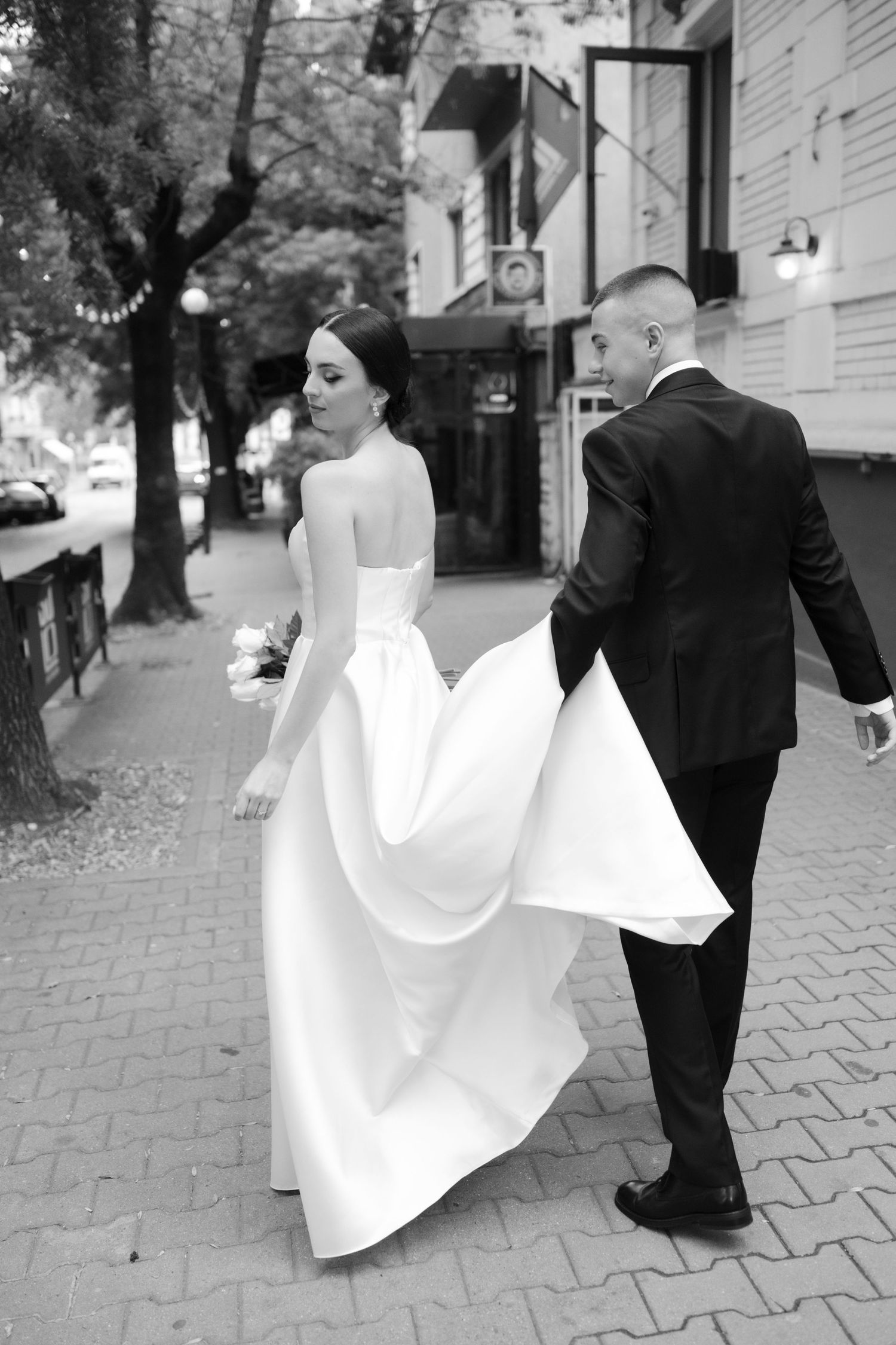 A series of black and white photos showing a bride in flowing white dress and groom walking along a paved path.