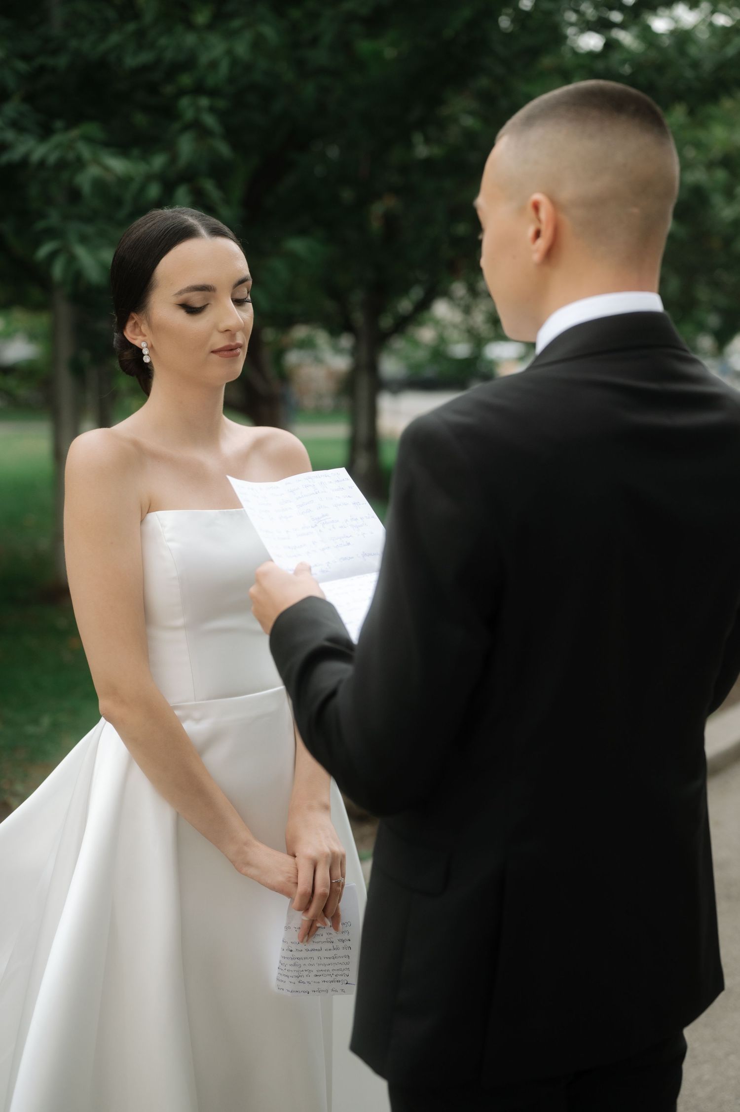 A couple in wedding attire shares an intimate moment outdoors with the bride in white and groom in black formal wear.