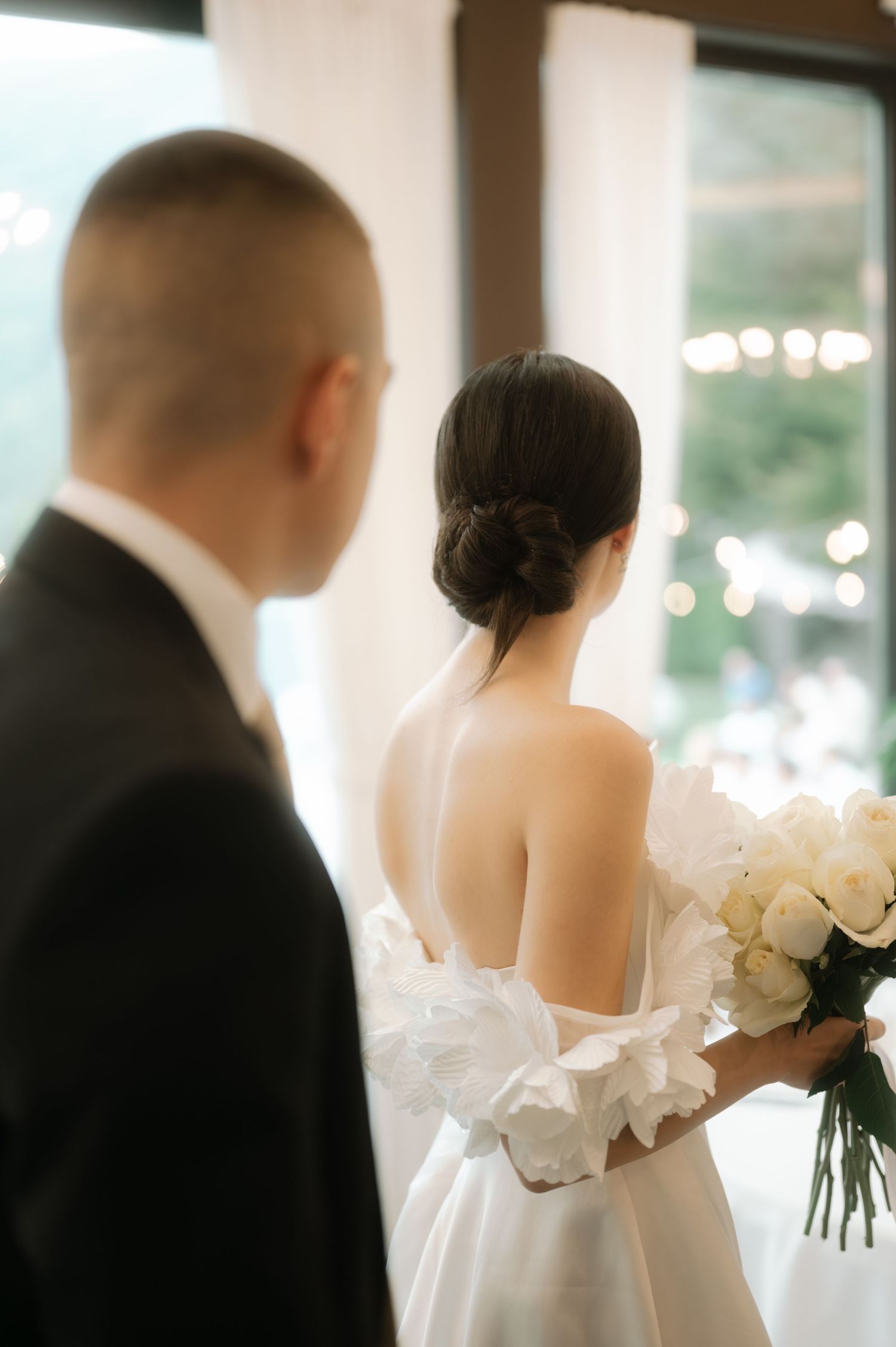 A romantic wedding scene showing a couple in black and white attire standing together with white floral bouquets.
