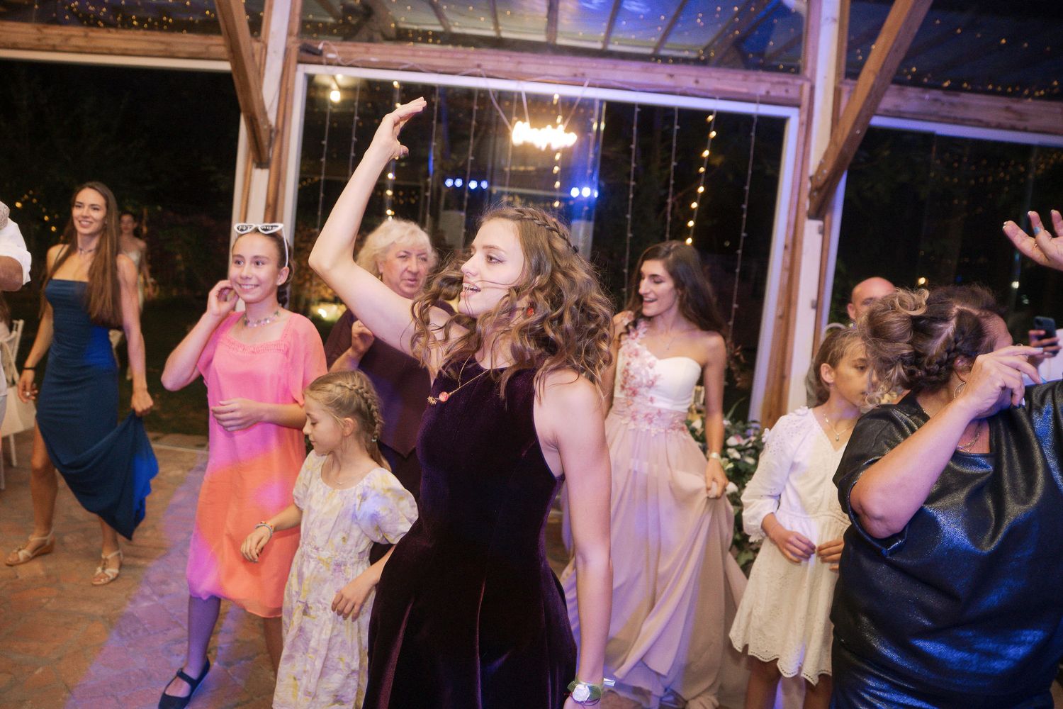 Wedding guests dancing and celebrating on a dance floor under string lights at an evening reception.