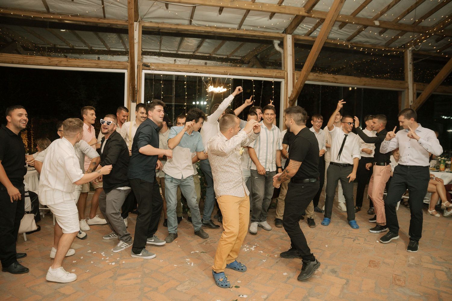 Guests performing line dance moves in formation on wooden floor at rustic indoor wedding reception.