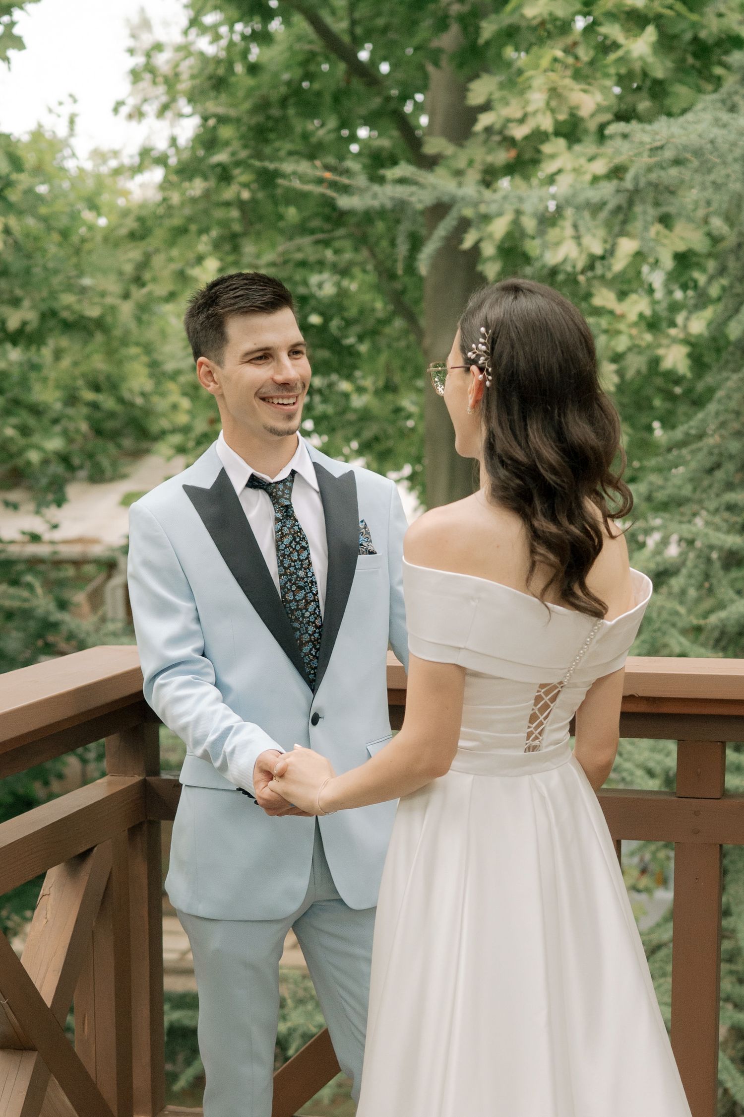 A couple shares a romantic moment on a wooden deck surrounded by lush green trees on their wedding day.