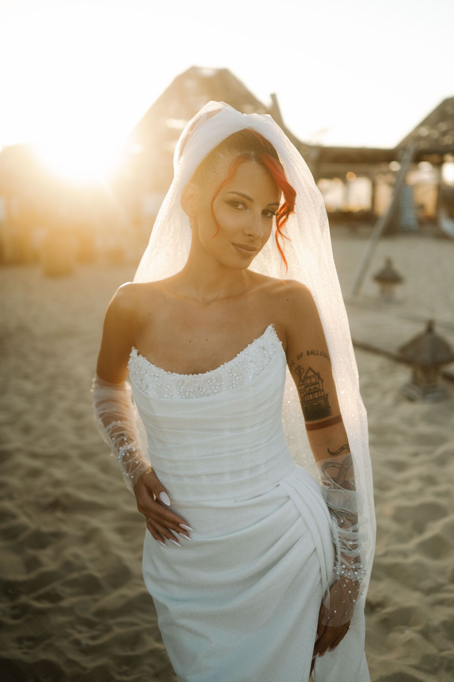 Ethereal beach bridal portraits at sunset showing a white wedding dress and tattoos against golden light.
