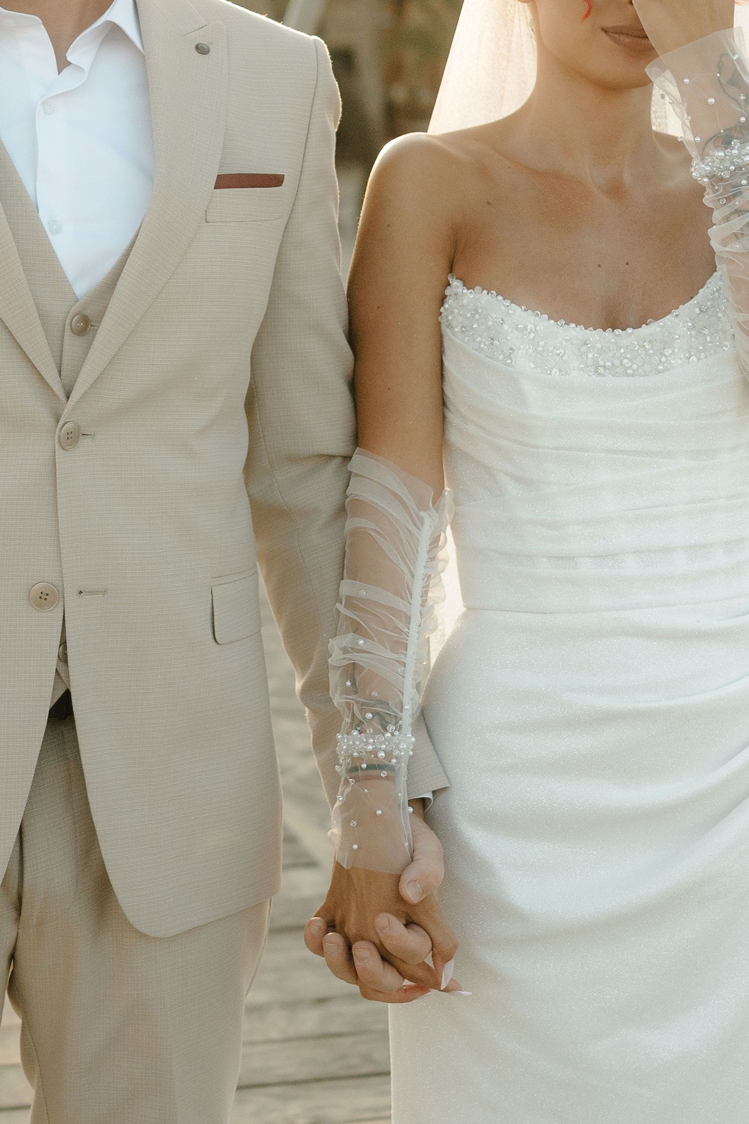 Wedding party members stand together wearing elegant white gowns and light beige suits in a formal group photo.