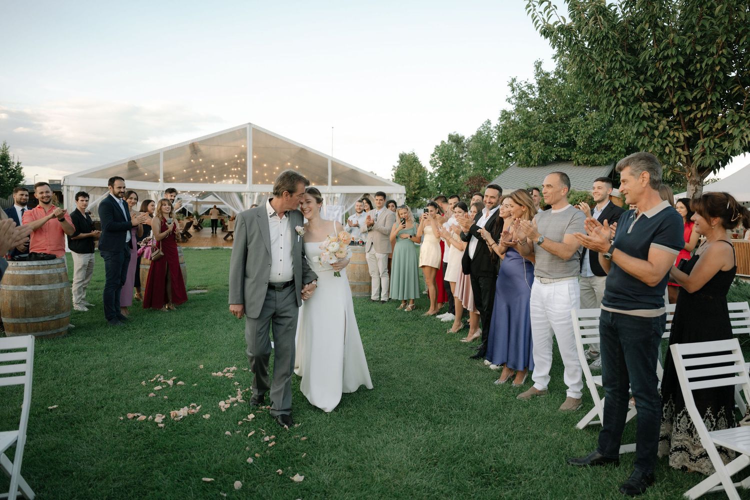 Wedding guests dancing together in a line on an outdoor lawn during a reception celebration.