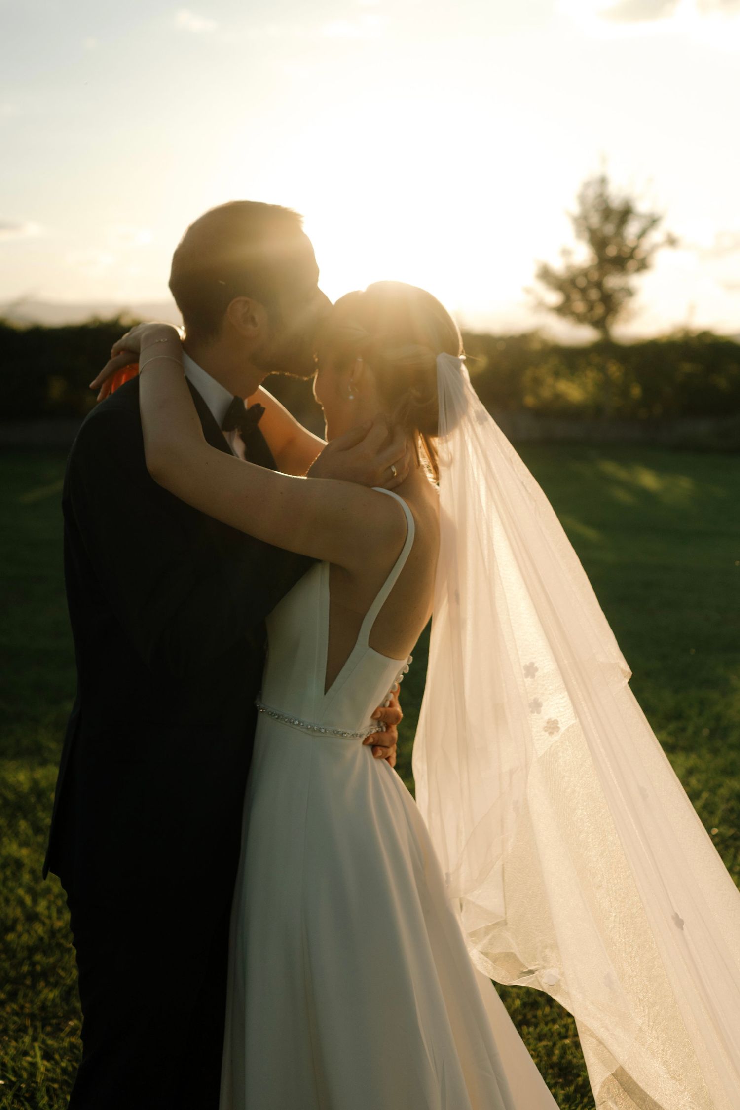 A romantic silhouette of a couple embracing during sunset with a flowing white wedding veil creating an ethereal scene.