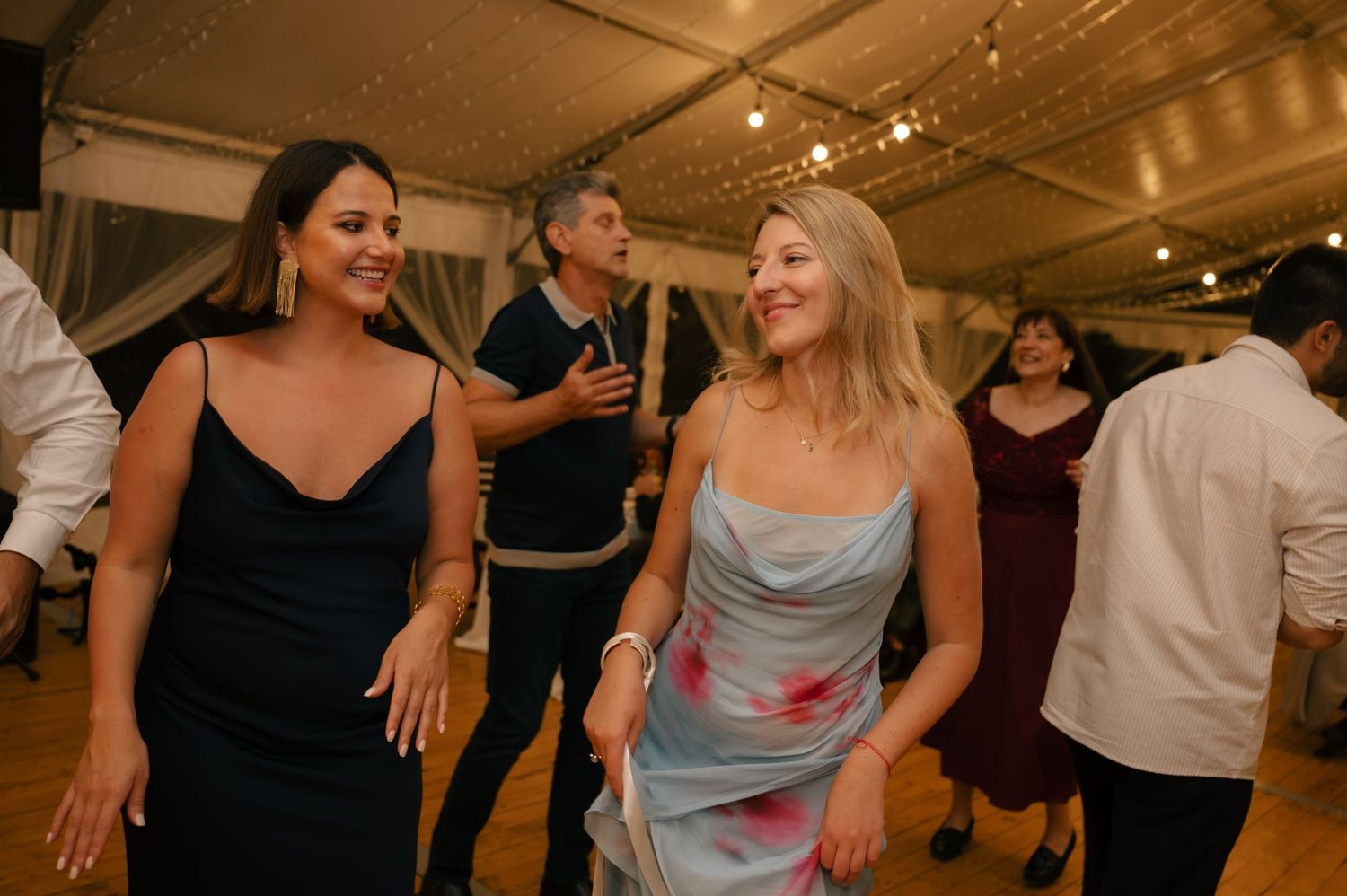 Guests dancing and celebrating at an indoor wedding reception with string lights overhead.