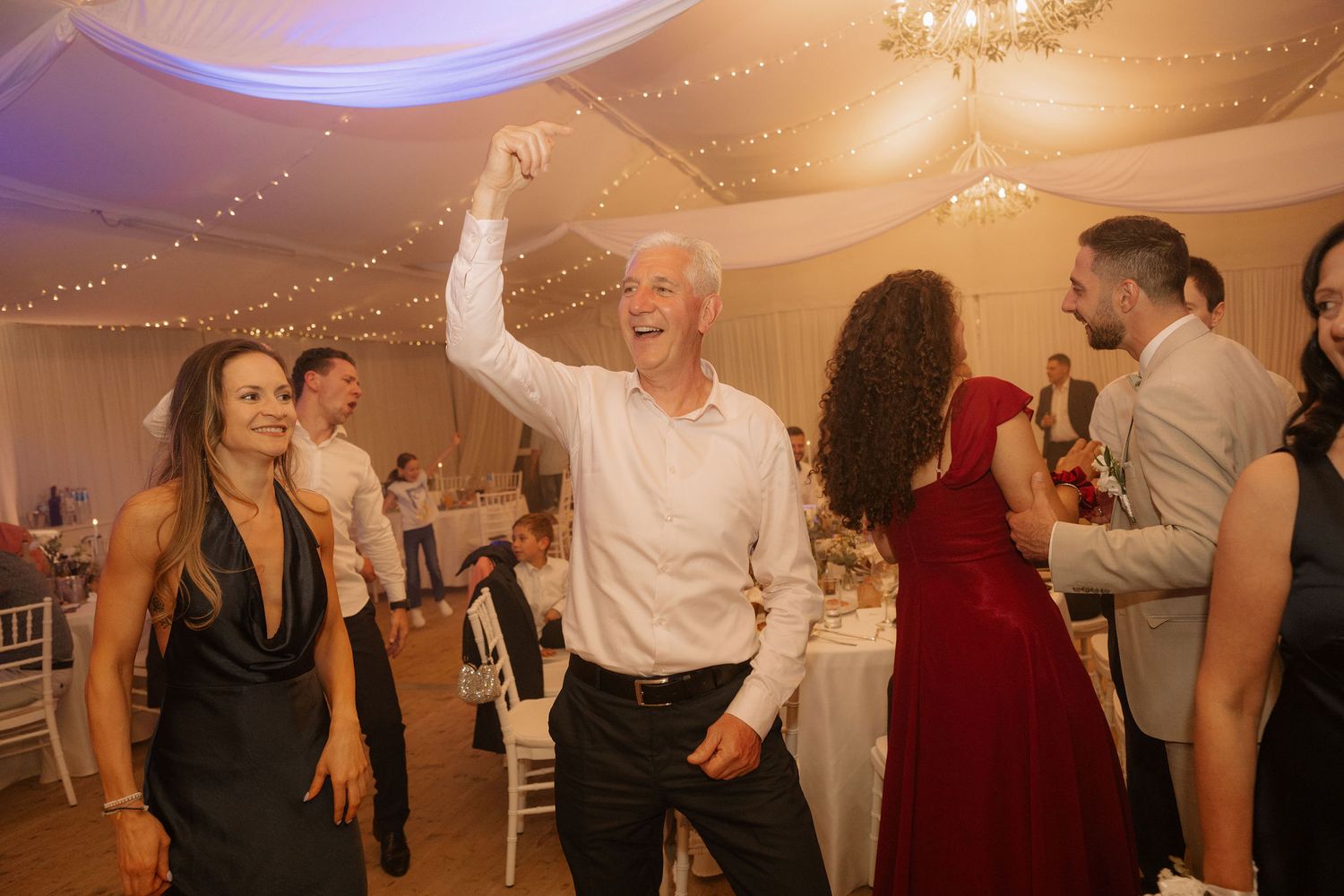 Guests dancing joyfully at an elegant wedding reception in a decorated marquee venue.