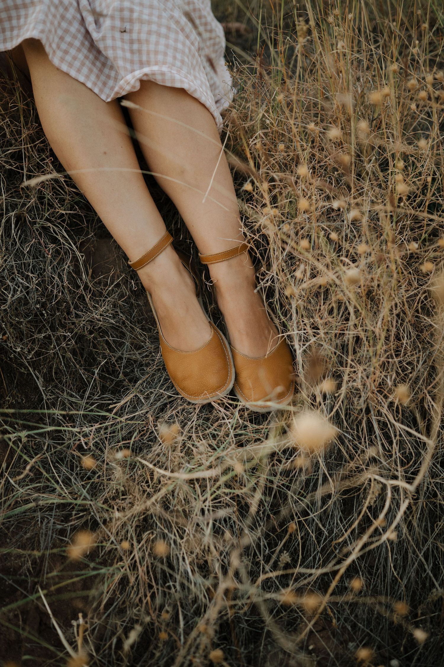 Brown leather mary jane shoes against dried grass and twigs in a rustic outdoor setting.