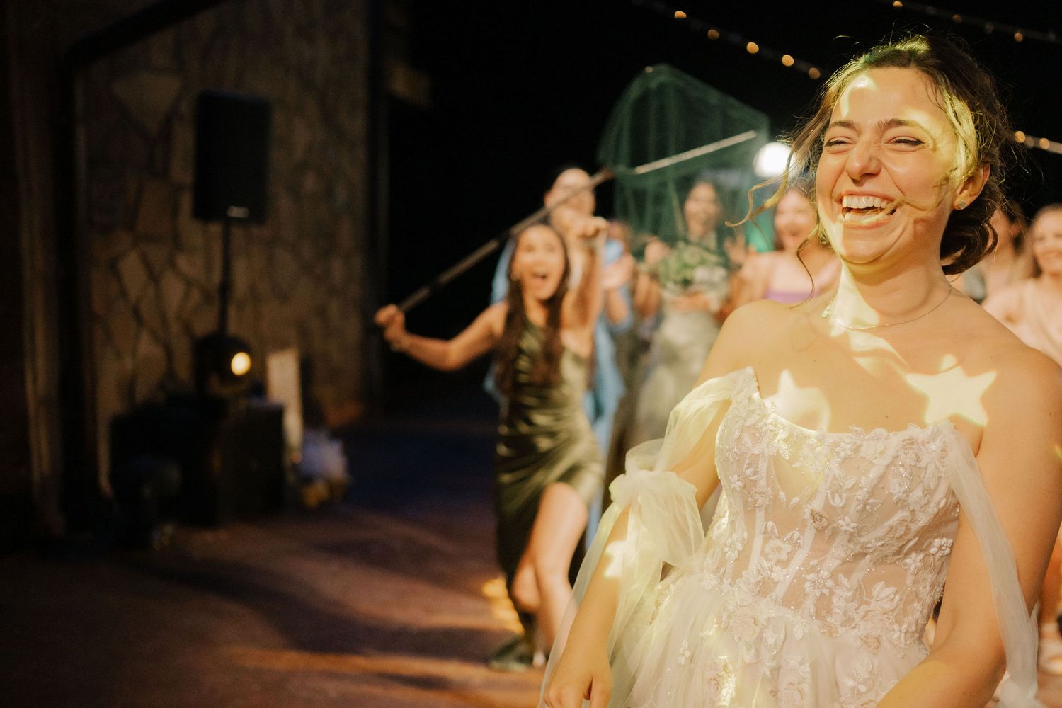A couple shares a romantic dance at their wedding reception in a dimly lit venue with fairy lights.