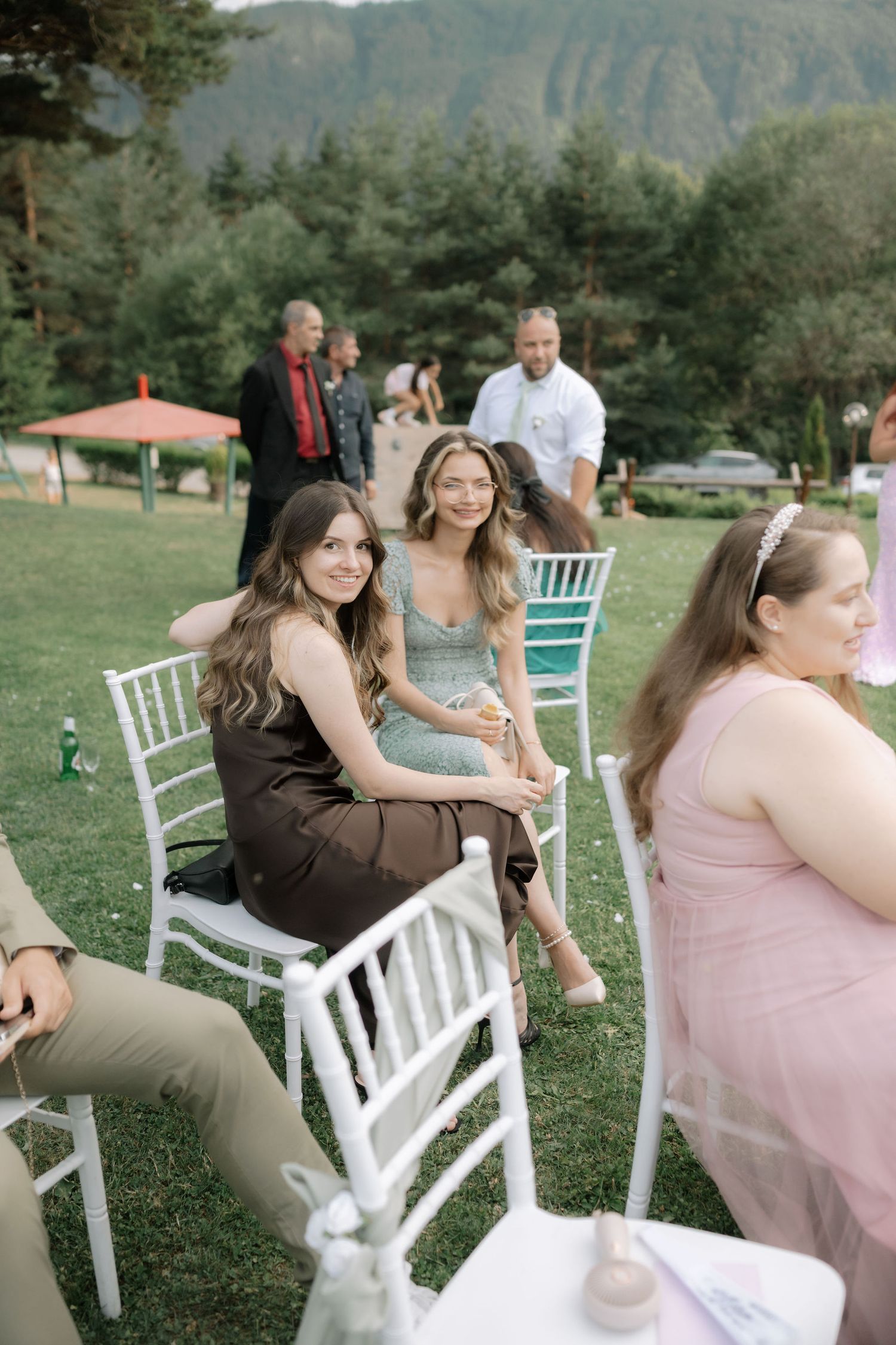 Wedding guests seated in white chairs on a grassy lawn with mountain views in the background.
