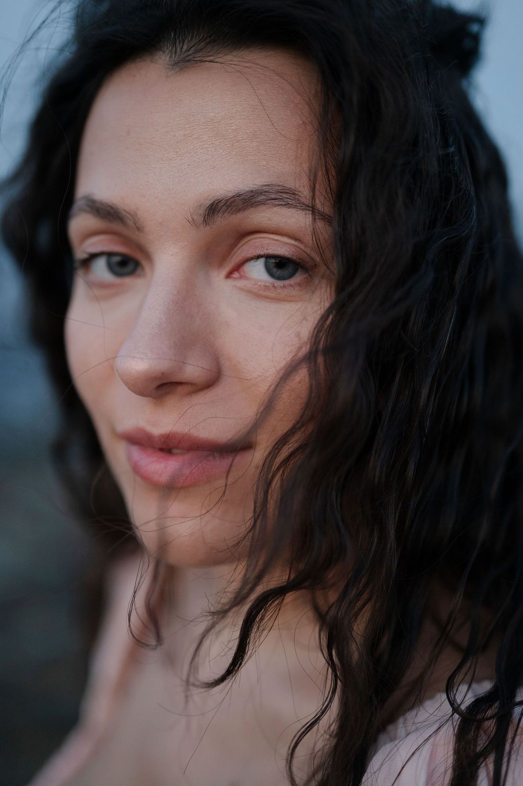 Close-up portrait of someone with dark wavy hair and a gentle smile against a blurred background.