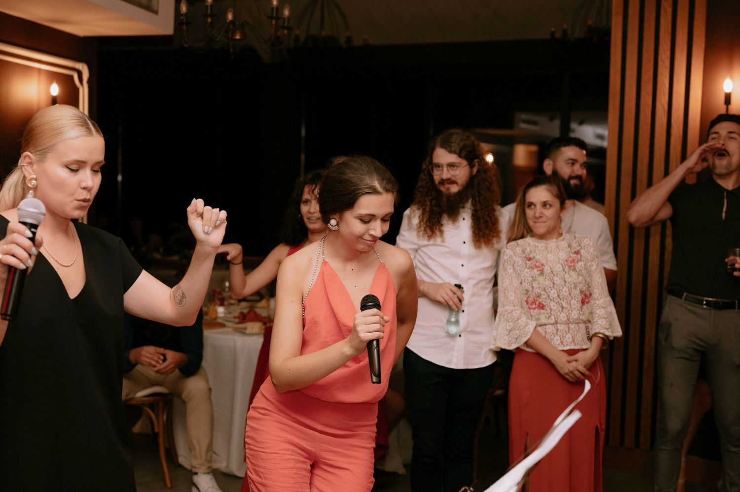 People dancing and celebrating at a wedding reception in a dimly lit venue with wooden paneled walls.
