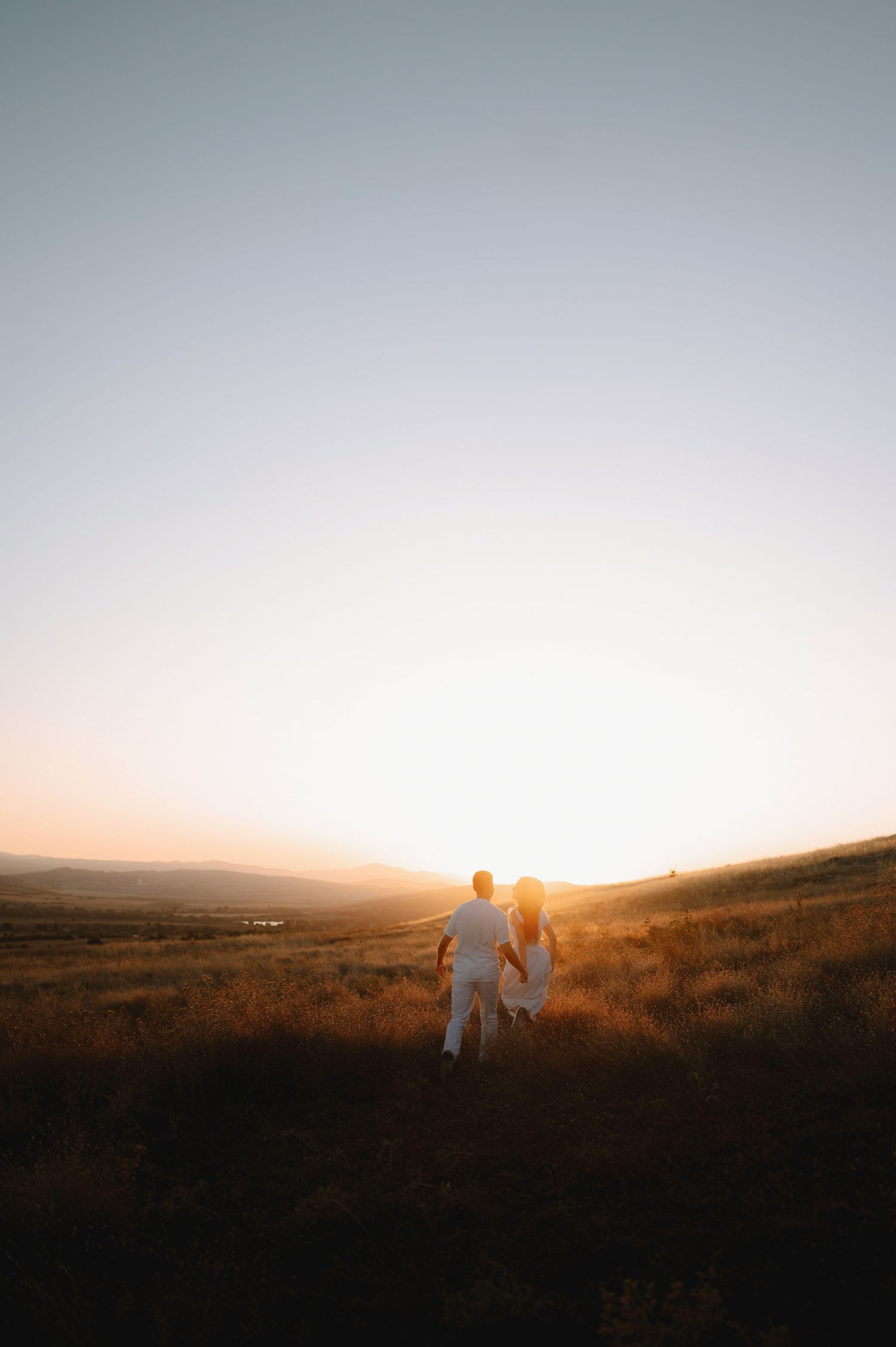 Silhouettes of people walking across rolling hills at sunset with warm golden light illuminating the landscape.