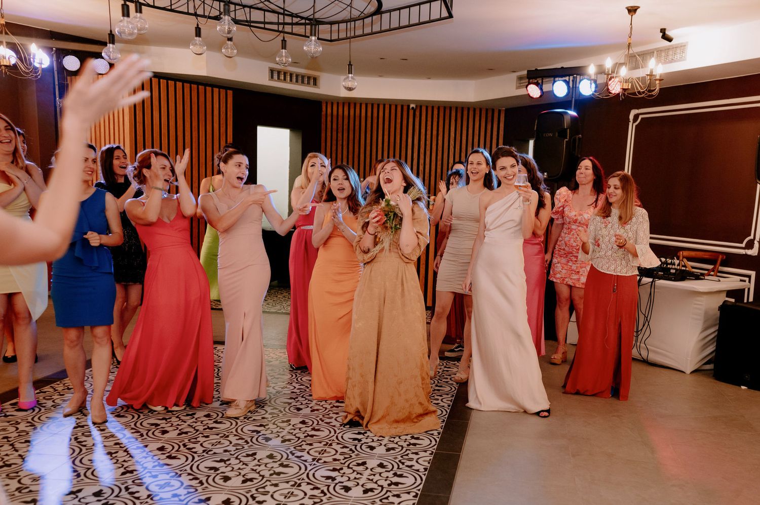Wedding guests dance and celebrate on a patterned ballroom floor during an evening reception.