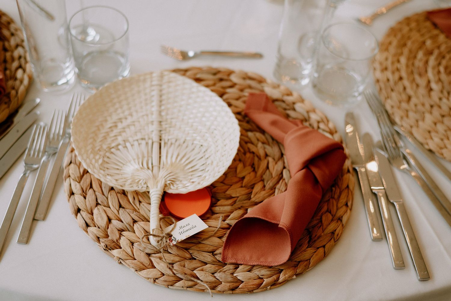 Elegant table setting with woven placemats, silverware, and white dishes in natural tones for a rustic dining experience.
