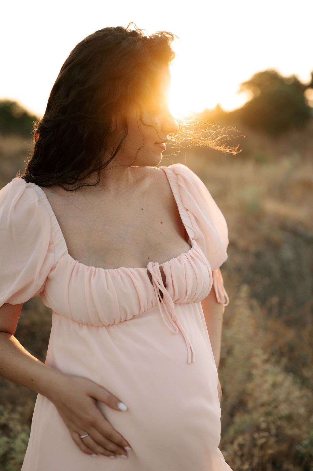 Woman in a white peasant dress standing in a golden field at sunset with soft glowing light.