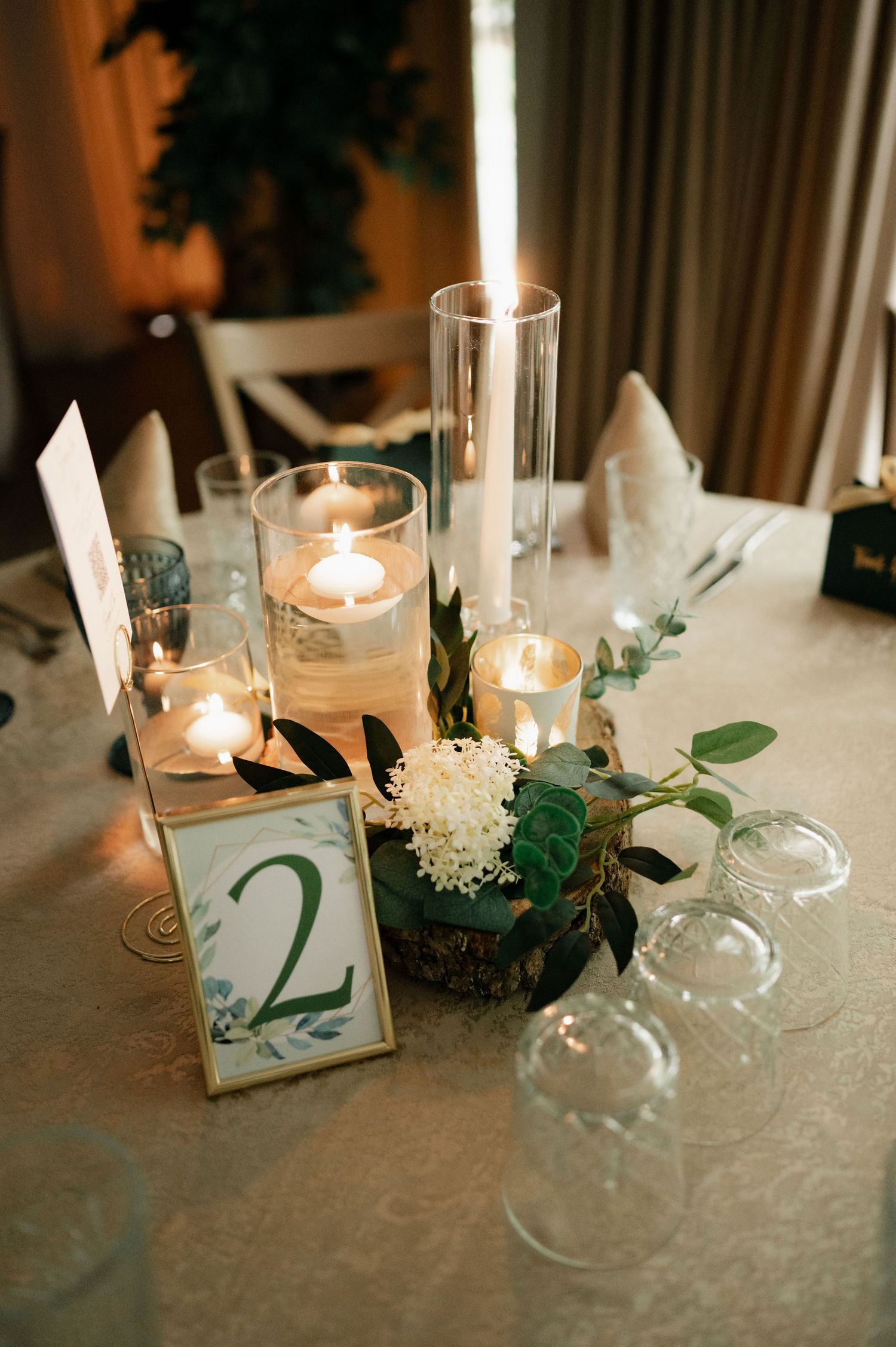 Elegant wedding table decor featuring lit candles, white flowers, and numbered table markers on a textured white tablecloth.
