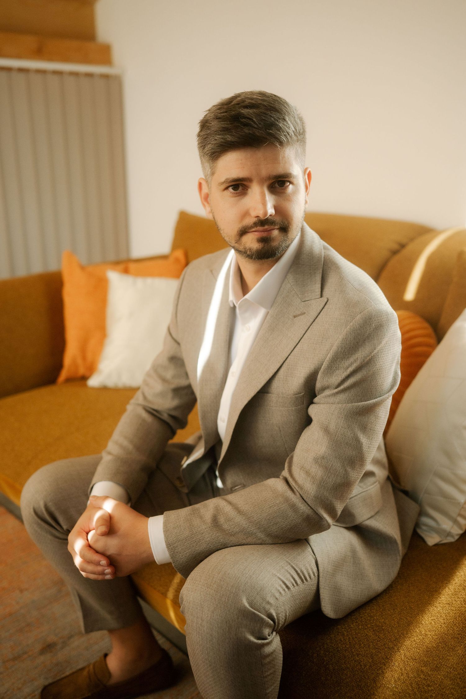 A person in a light gray suit reclines on an orange couch in a modern interior setting.
