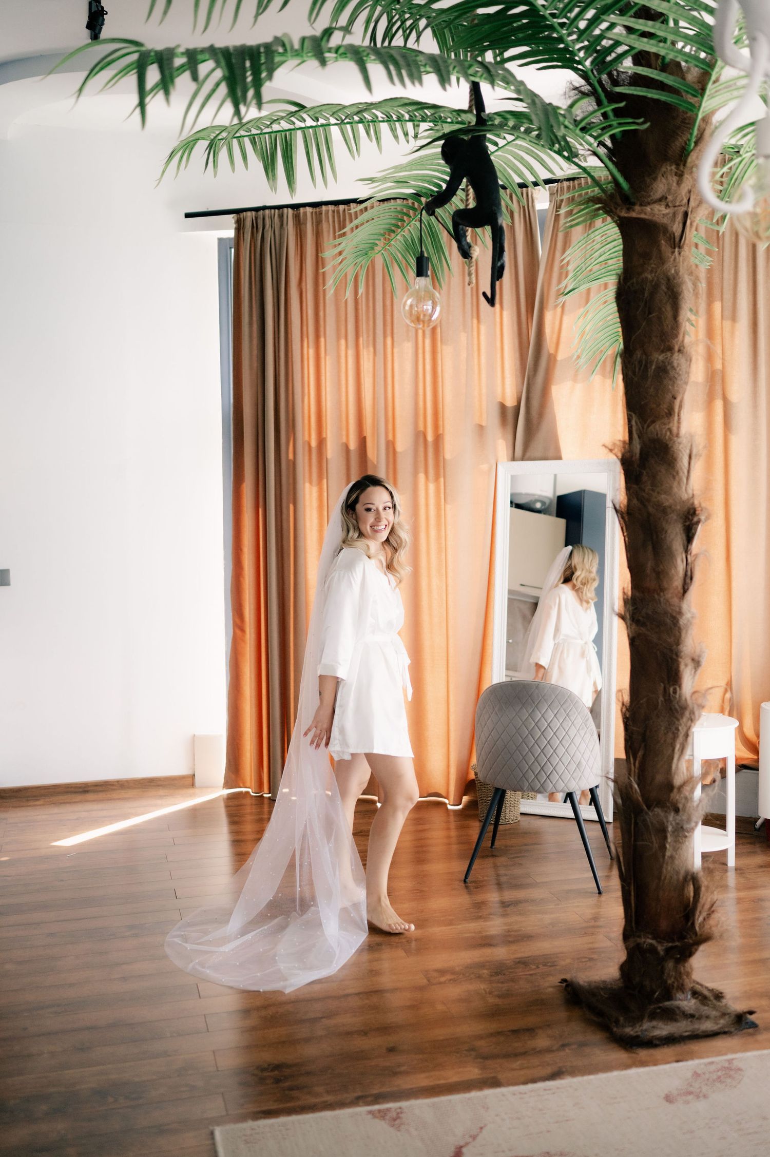 A flowing white bridal veil catches sunlight in a room with hardwood floors and a palm tree.