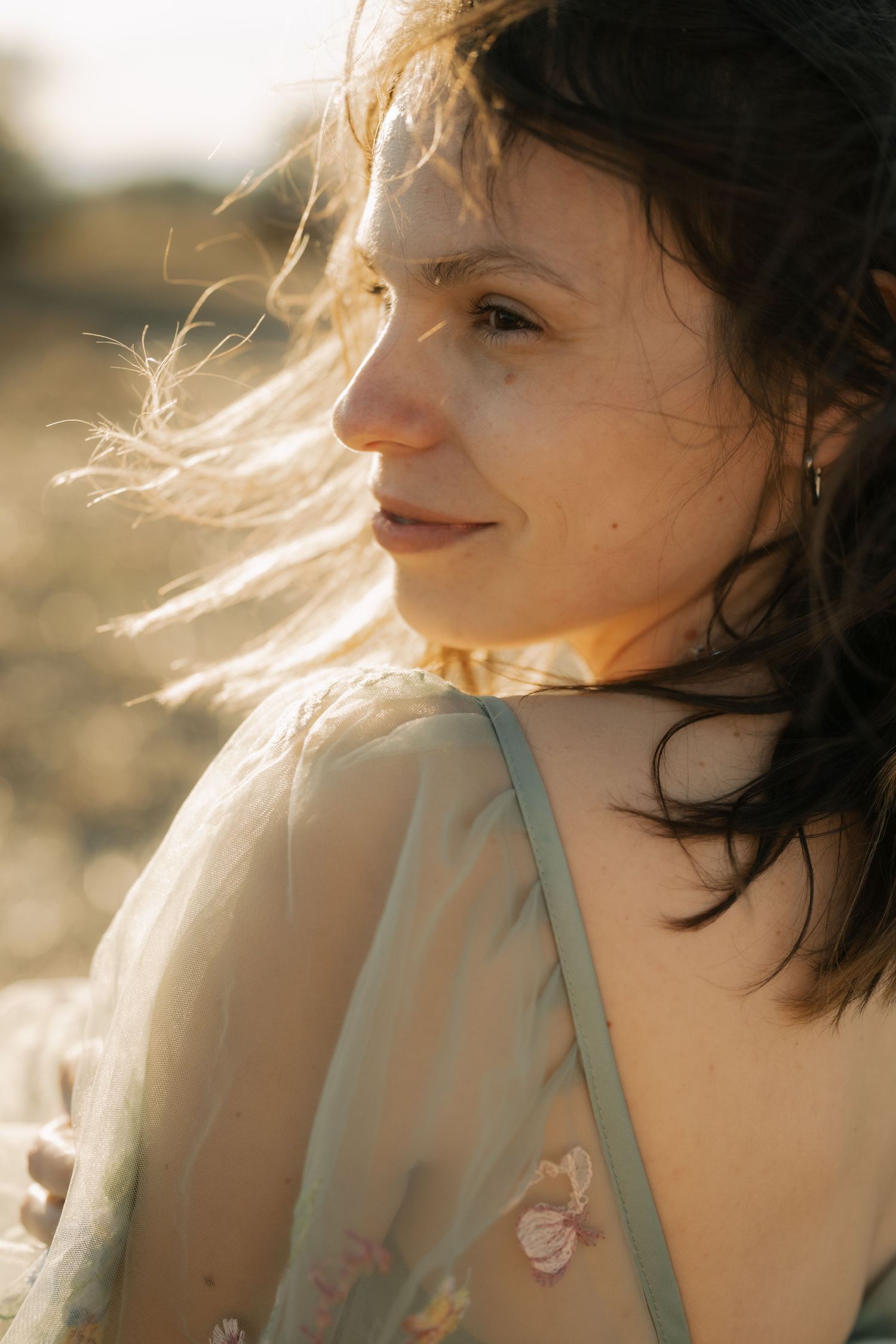 Ethereal backlit portrait in soft golden sunlight showing windswept hair and delicate features against a dreamy natural backdrop.
