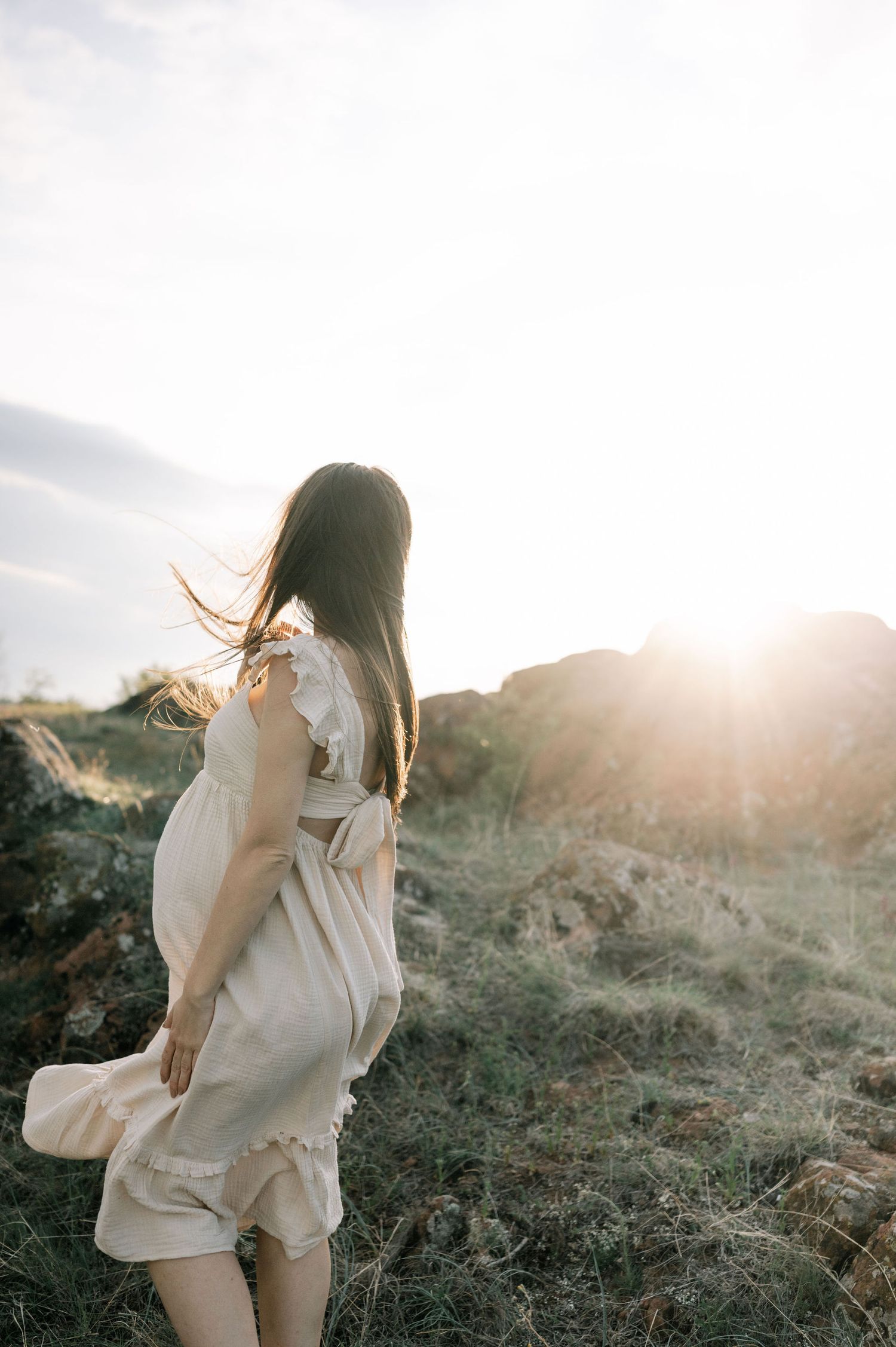 A person in a light-colored dress stands against a dramatic mountain backdrop during sunset.