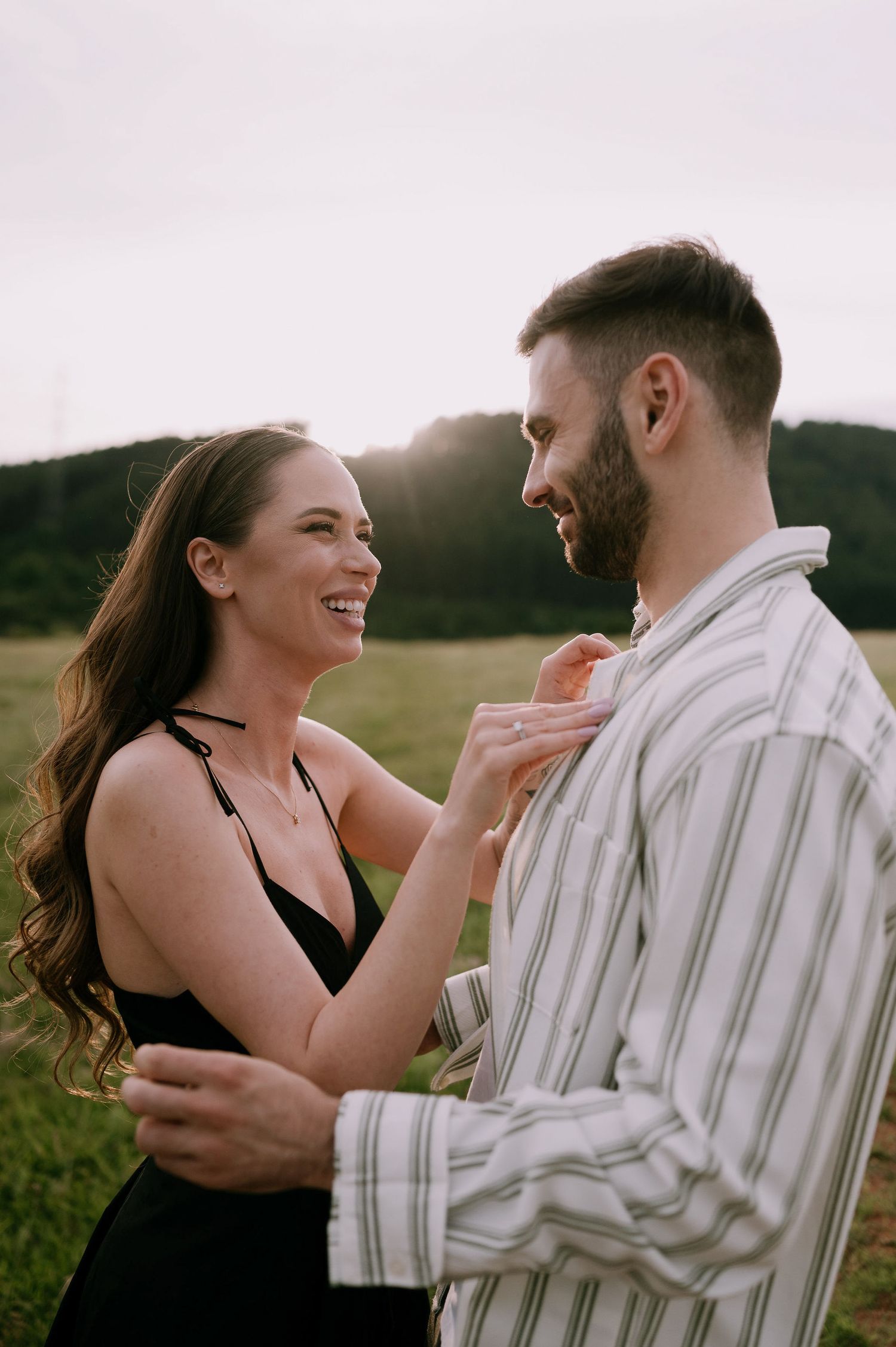 A couple shares joyful laughter while embracing in a scenic outdoor setting during golden hour.