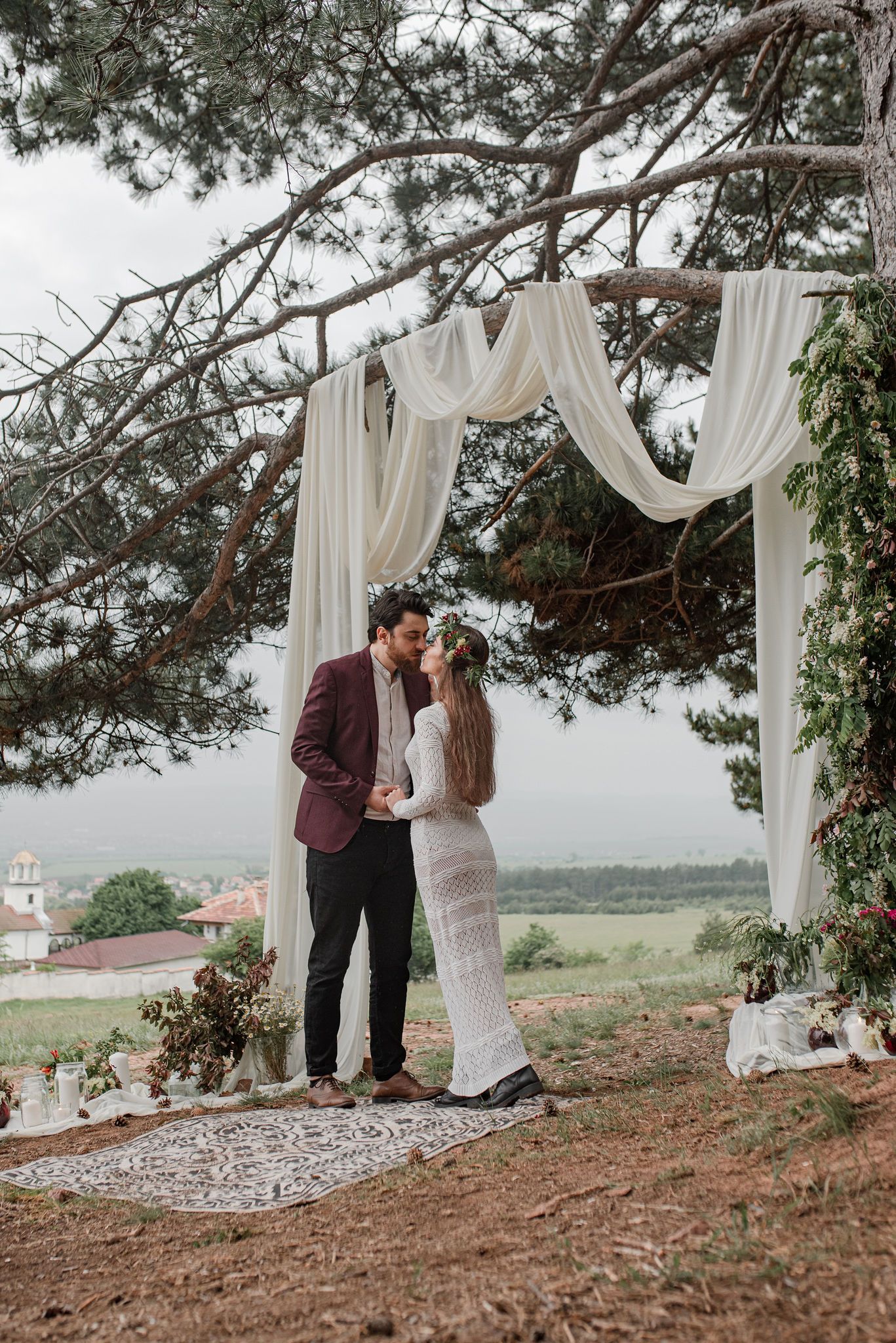 A romantic couple shares a tender moment under white fabric draping and pine trees with a scenic landscape view.