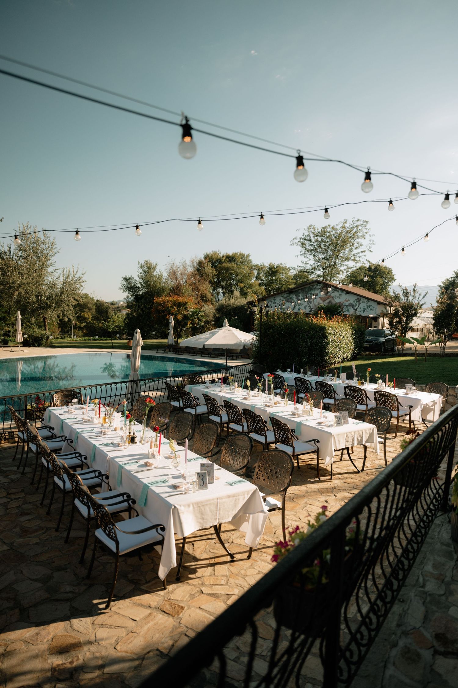 Outdoor wedding reception setup with long tables and string lights overlooking a scenic view at sunset.
