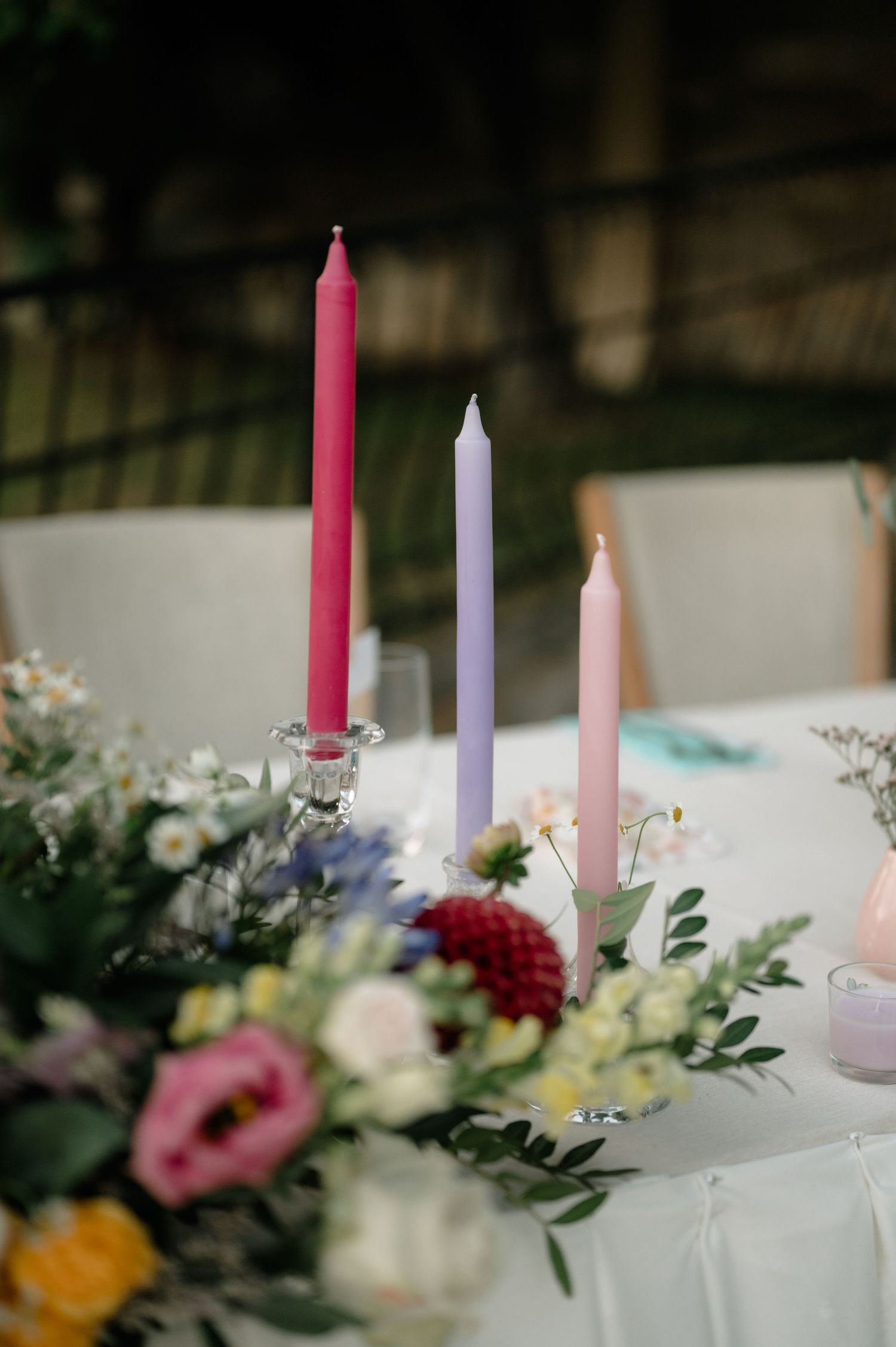 Elegant table setting with pink, purple and white taper candles surrounded by fresh flowers and greenery.