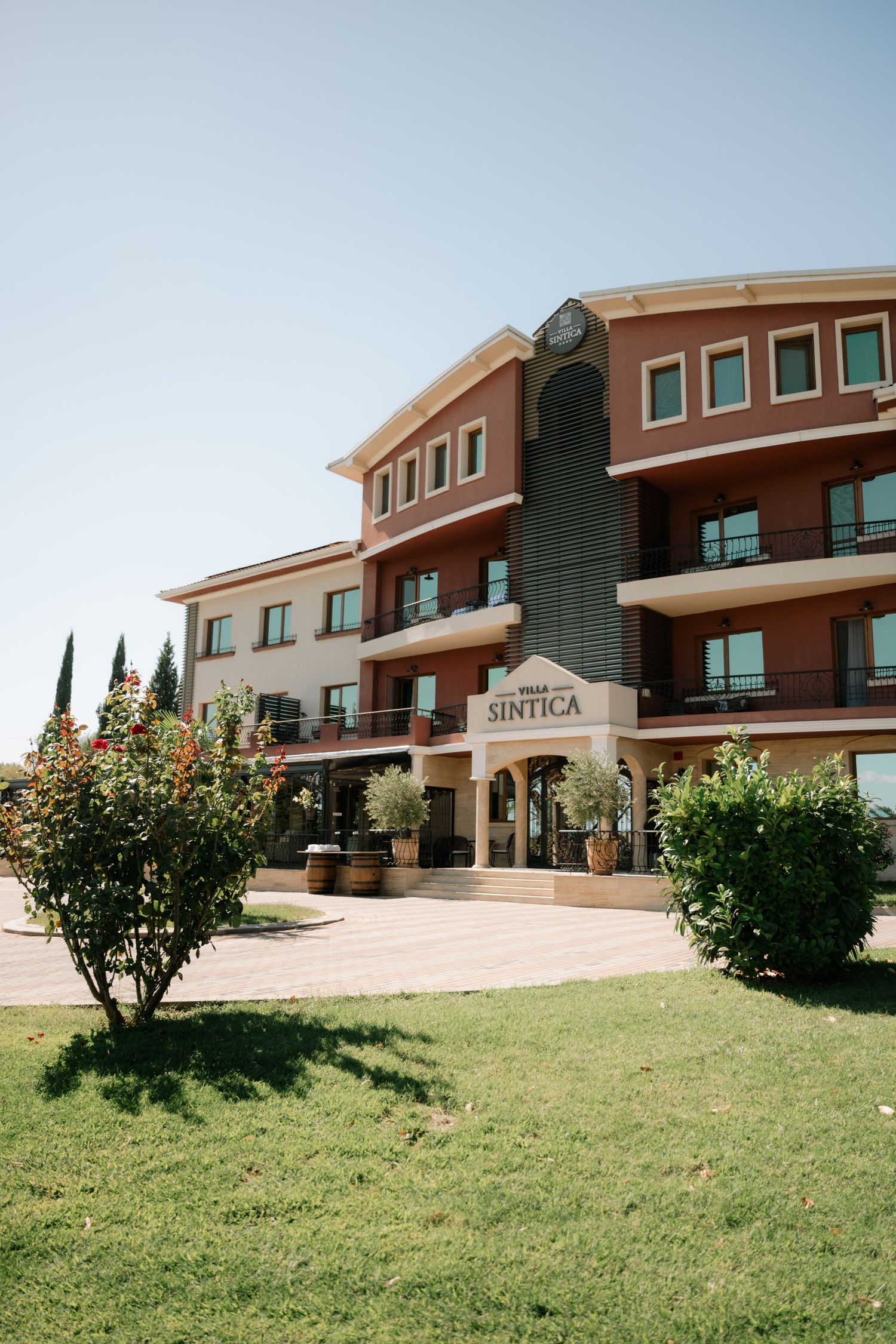 Modern commercial building complex with tan and brown exterior features curved architecture and landscaped lawn.