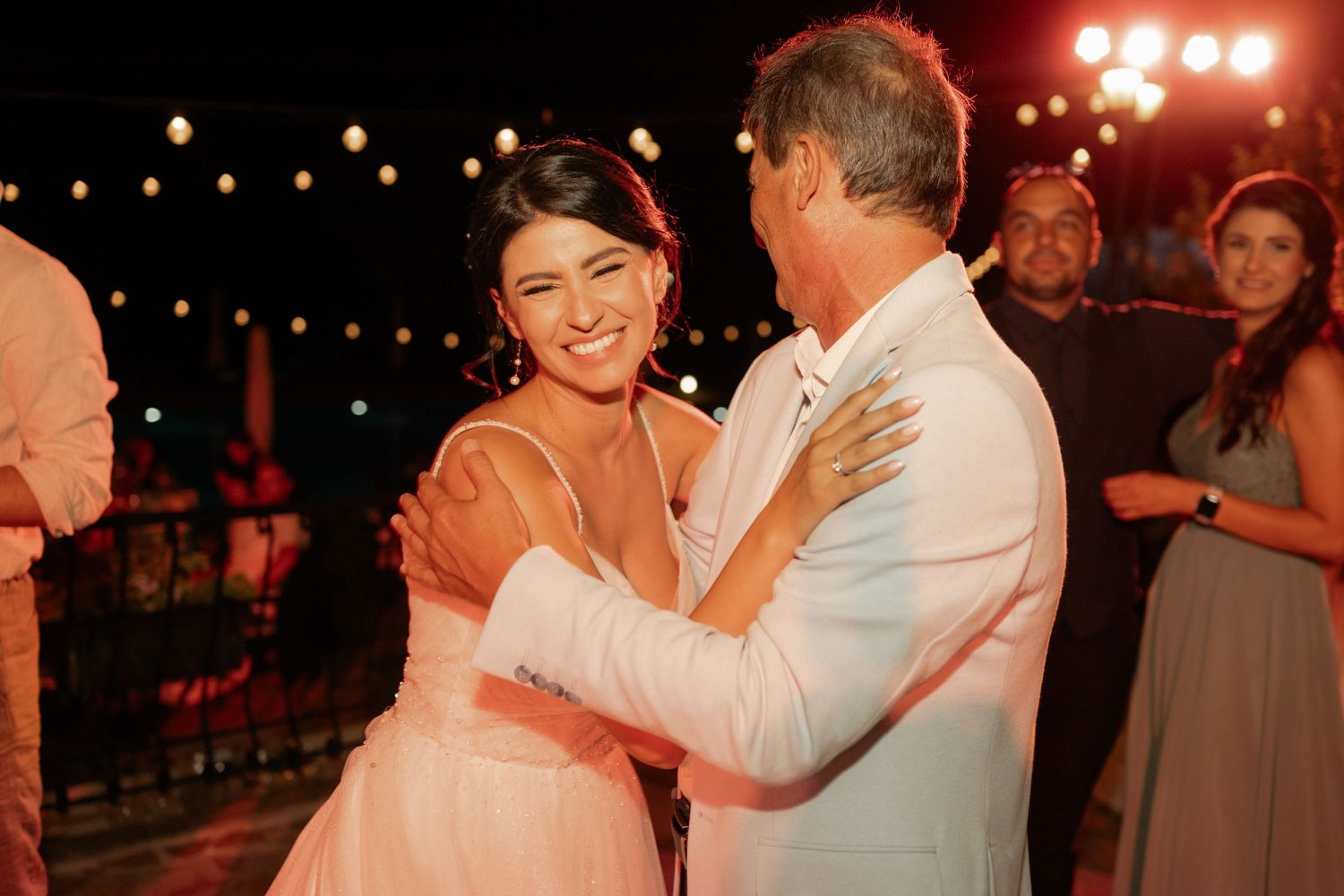 A couple dances together at an evening reception with string lights and warm lighting in the background.