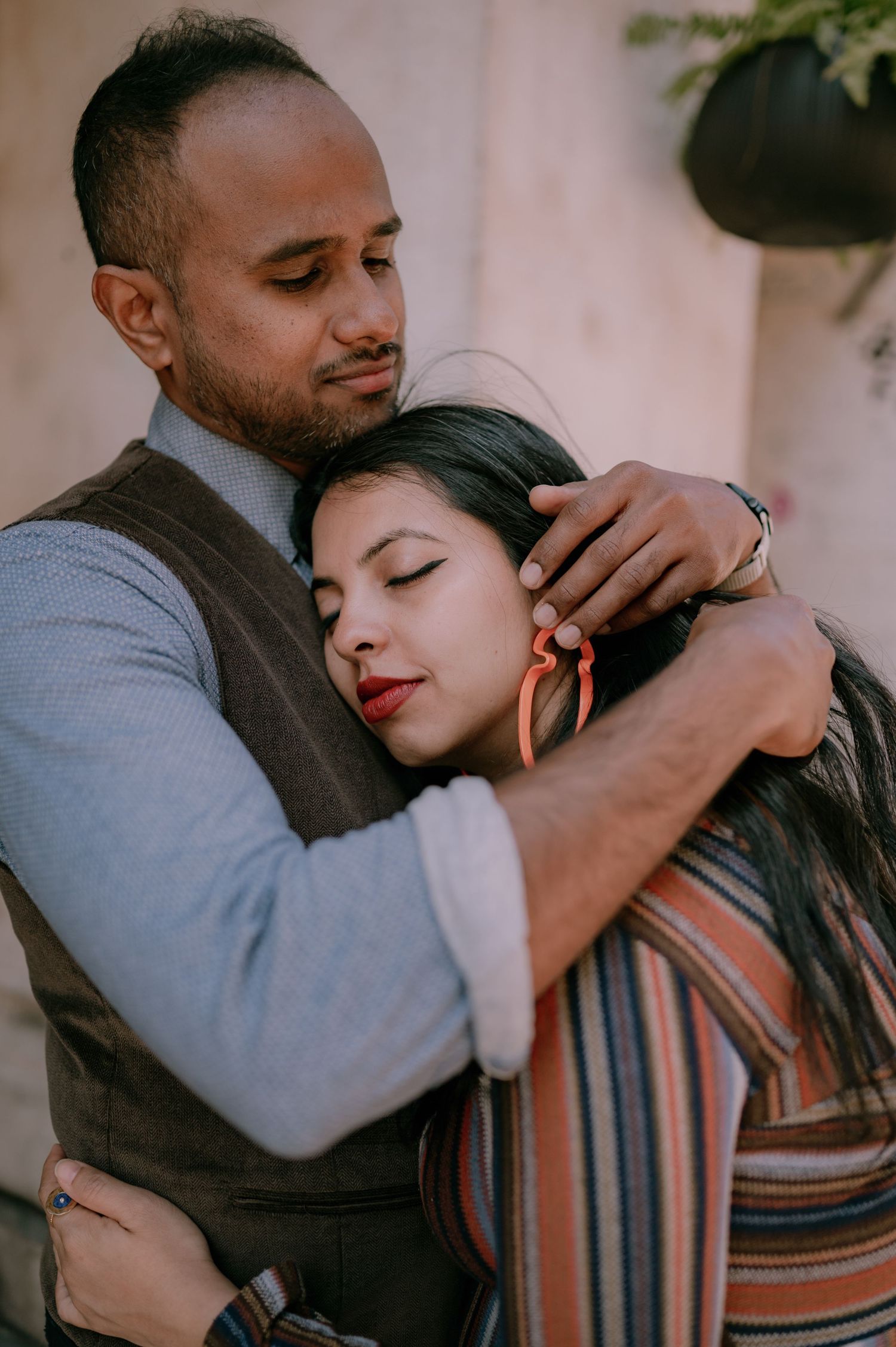 A man tenderly embraces a woman, holding her close as she rests her head on his chest with eyes closed.