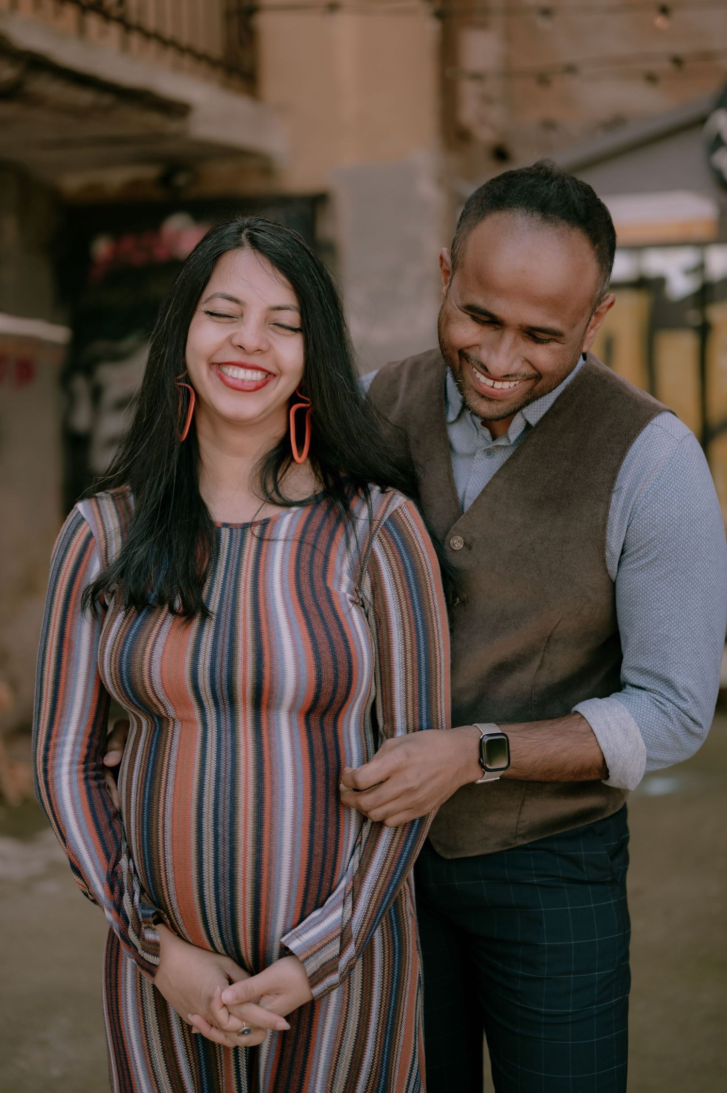Smiling pregnant woman in striped dress with partner outdoors during maternity photoshoot.