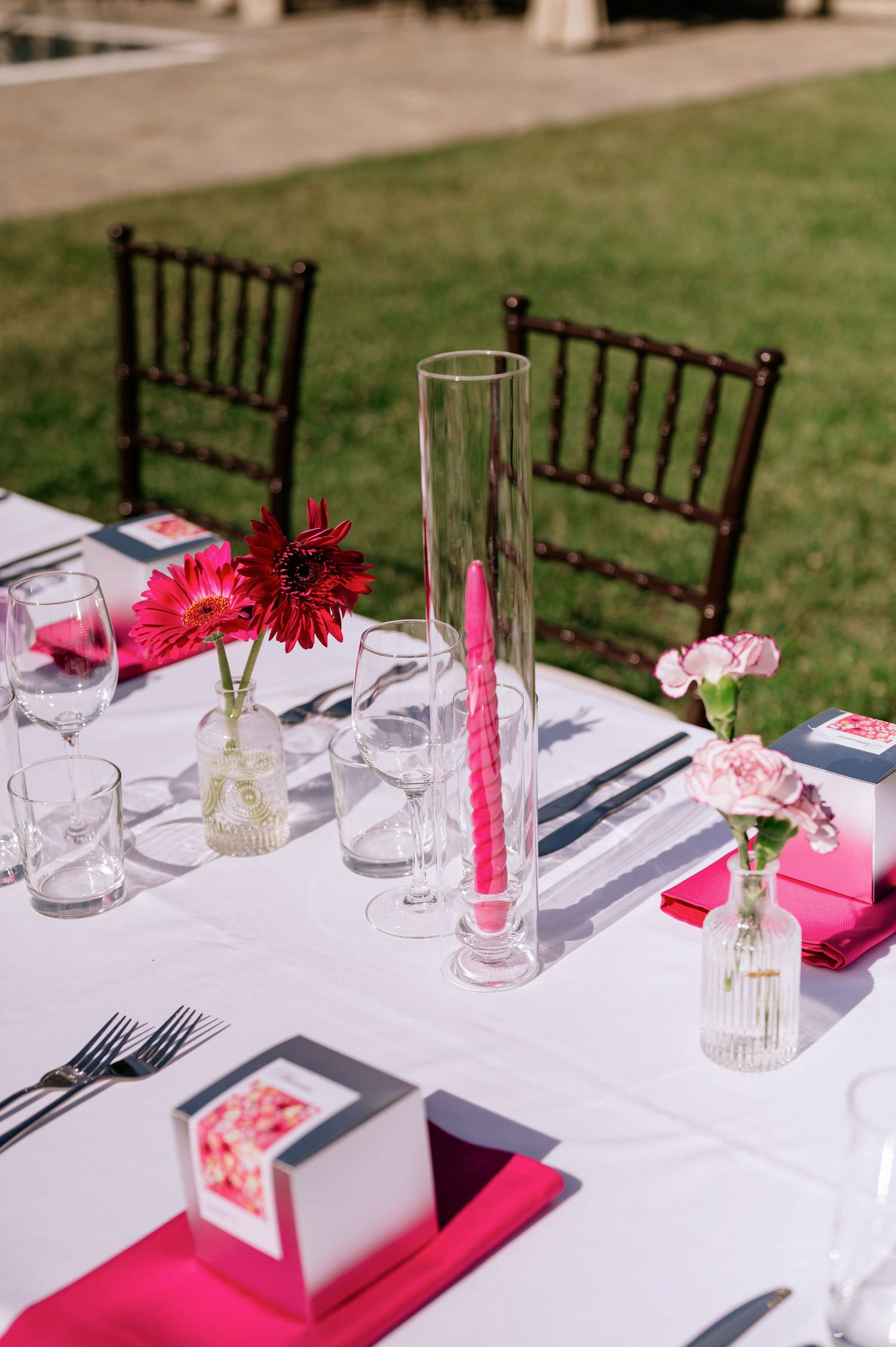 Elegant table setting with red flowers, crystal glasses, and dark wooden chairs.