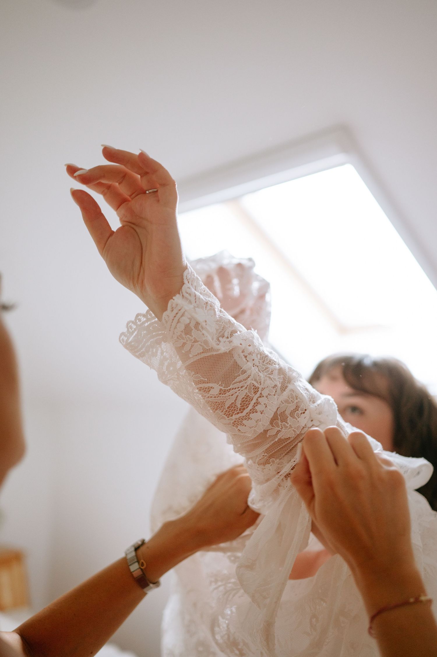 Hands in lace sleeves reaching upward against a bright white background.
