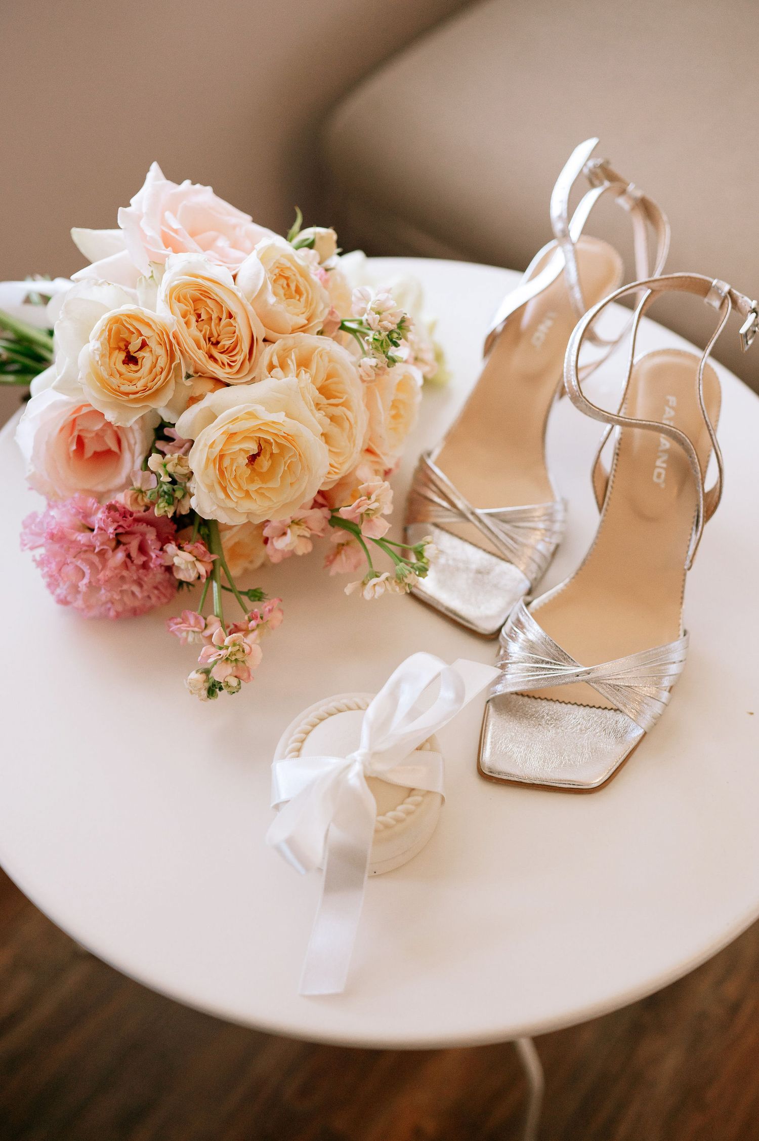 Elegant bridal shoes and peachy floral arrangement on white accent table.