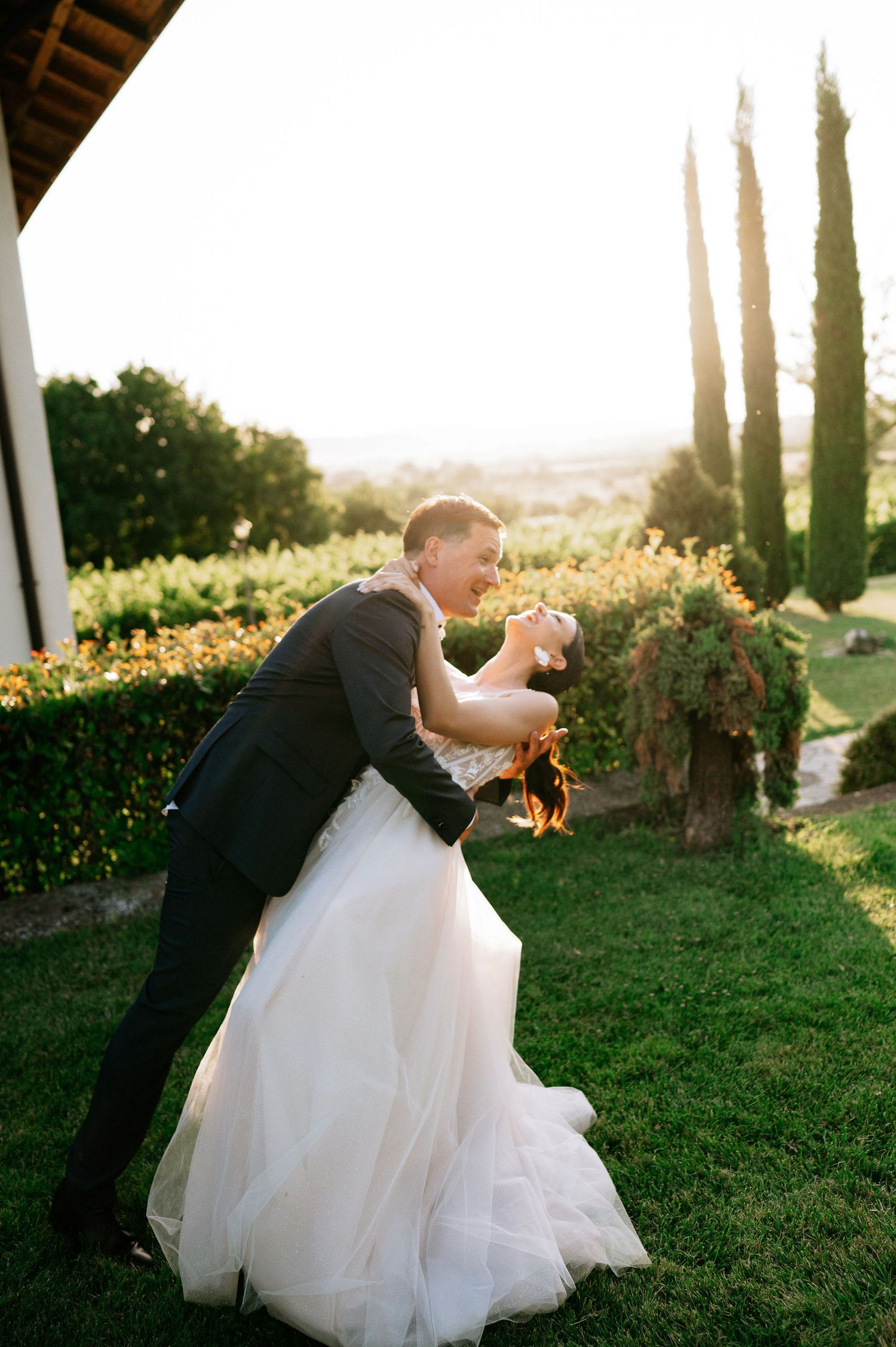 Elegant wedding couple performs dramatic dip pose during sunset photoshoot.